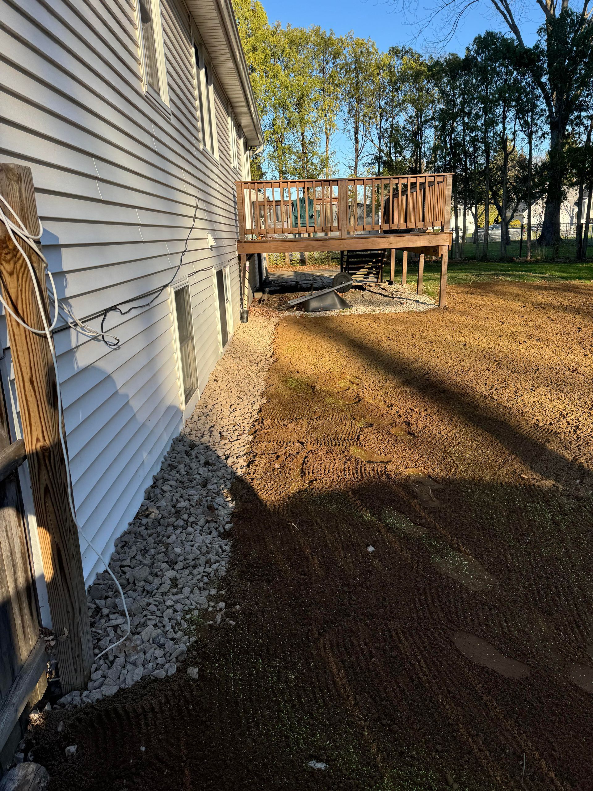Side of a house with gravel border and wooden deck in a grassy yard.