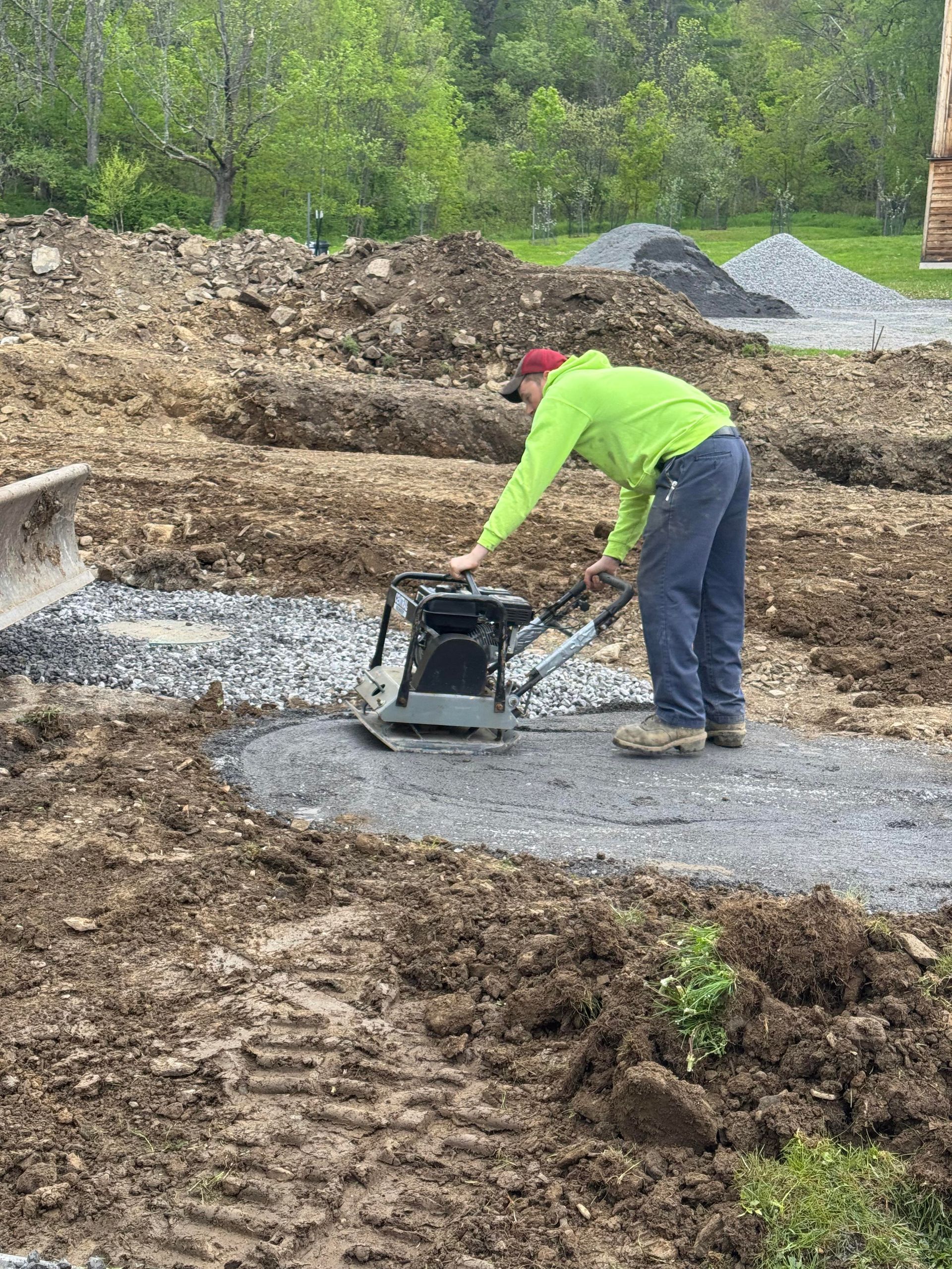 Man compacting gravel with a plate compactor on a construction site.