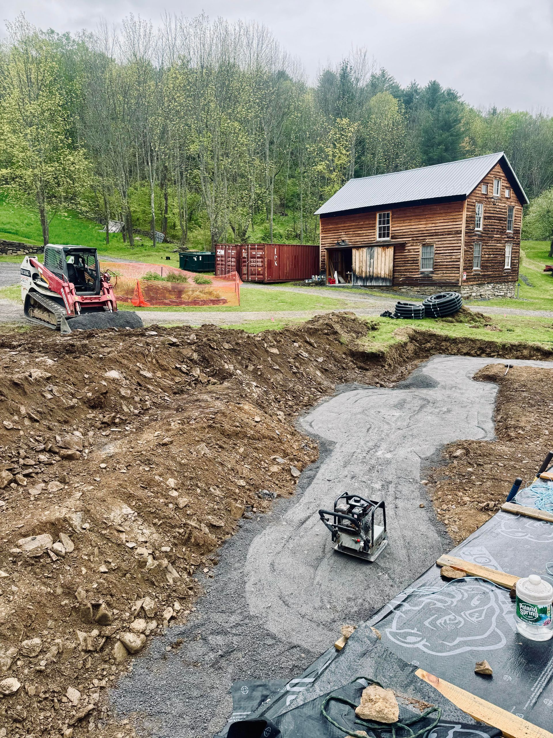 Construction site with a foundation trench, compacting machine, and a small wooden cabin.