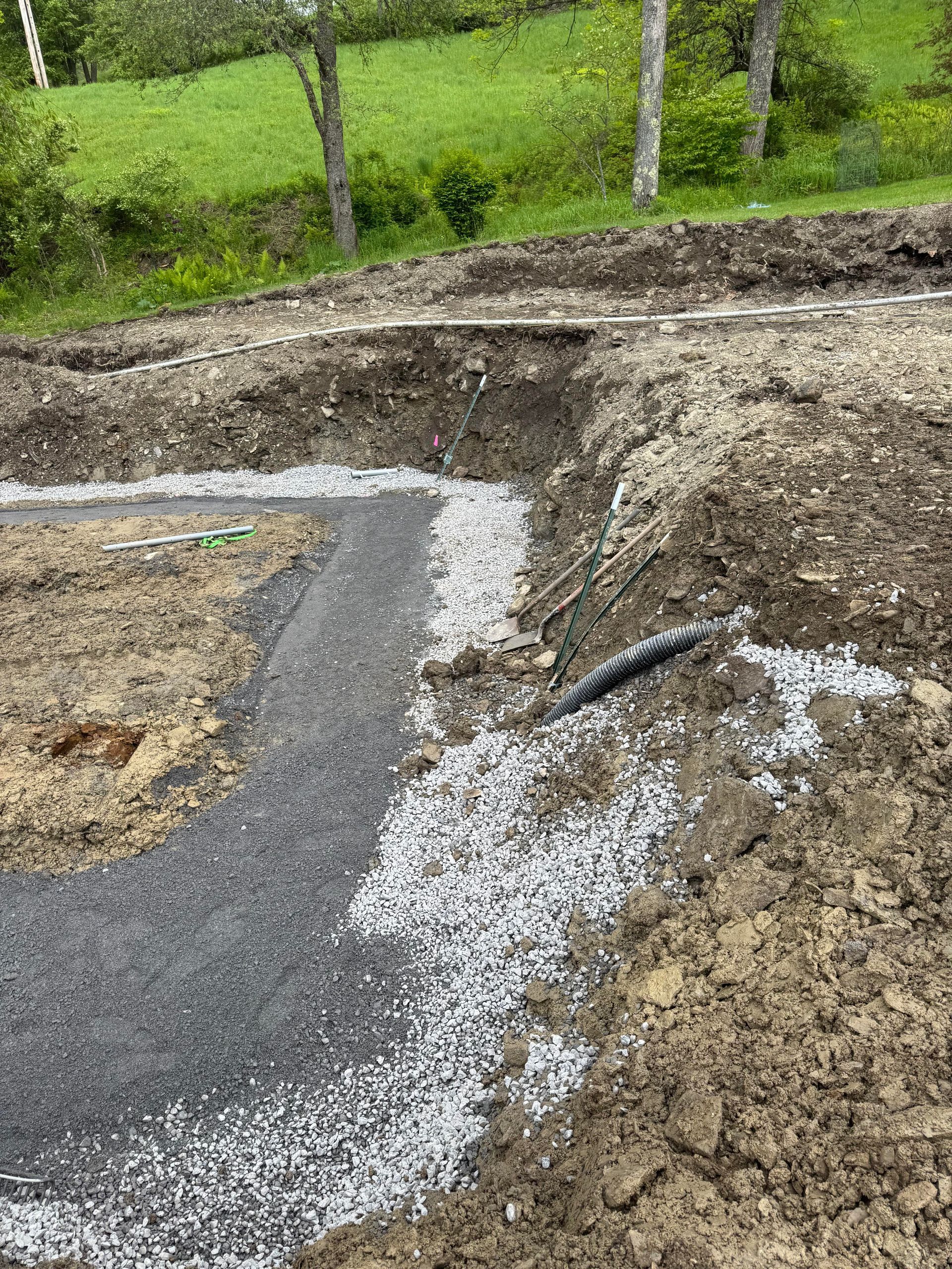 Gravel path laid in a freshly dug earthen area, leading toward a grassy hillside with trees.