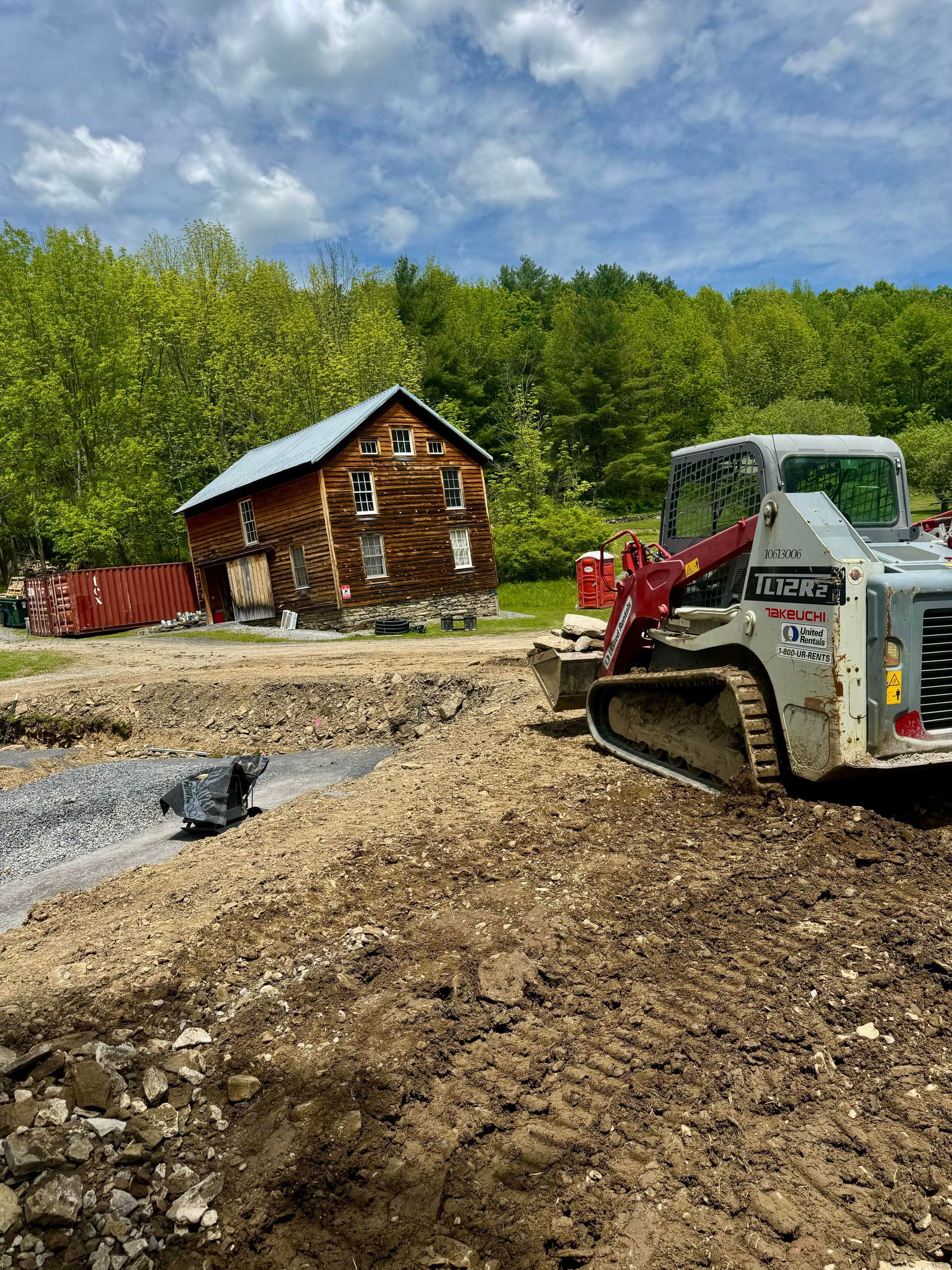 Construction site with log cabin in the background, a small machine digging in the dirt.
