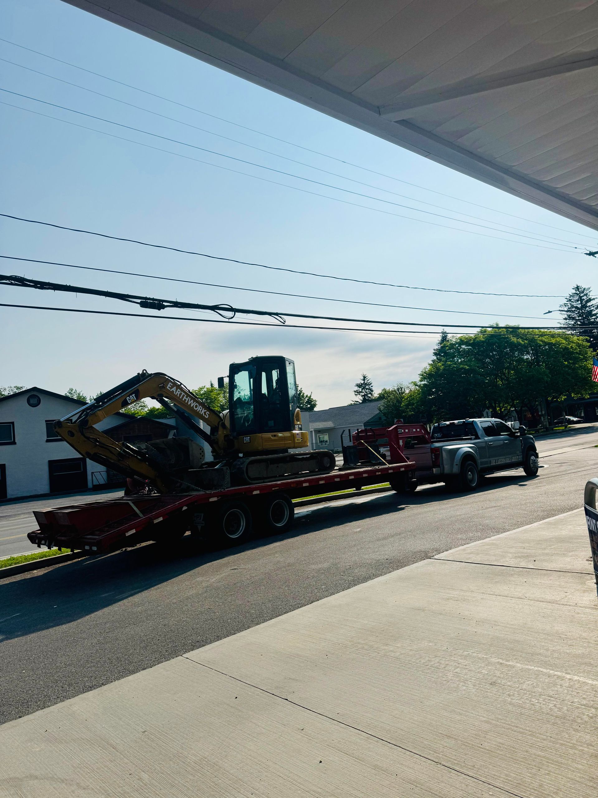 Excavator on a trailer being pulled by a truck on a street on a sunny day.