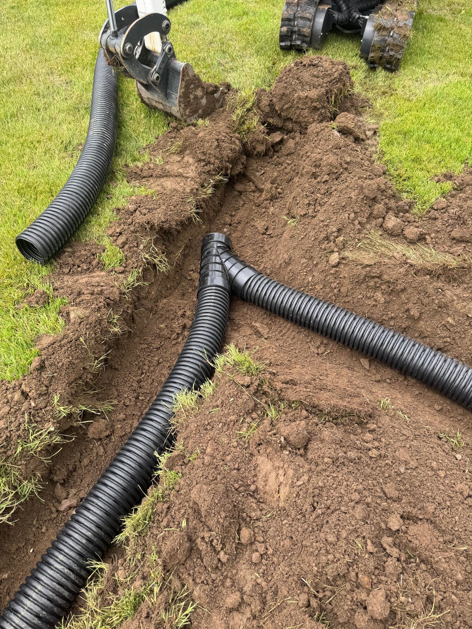 Black corrugated drainage pipes installed in a trench in a grassy yard.