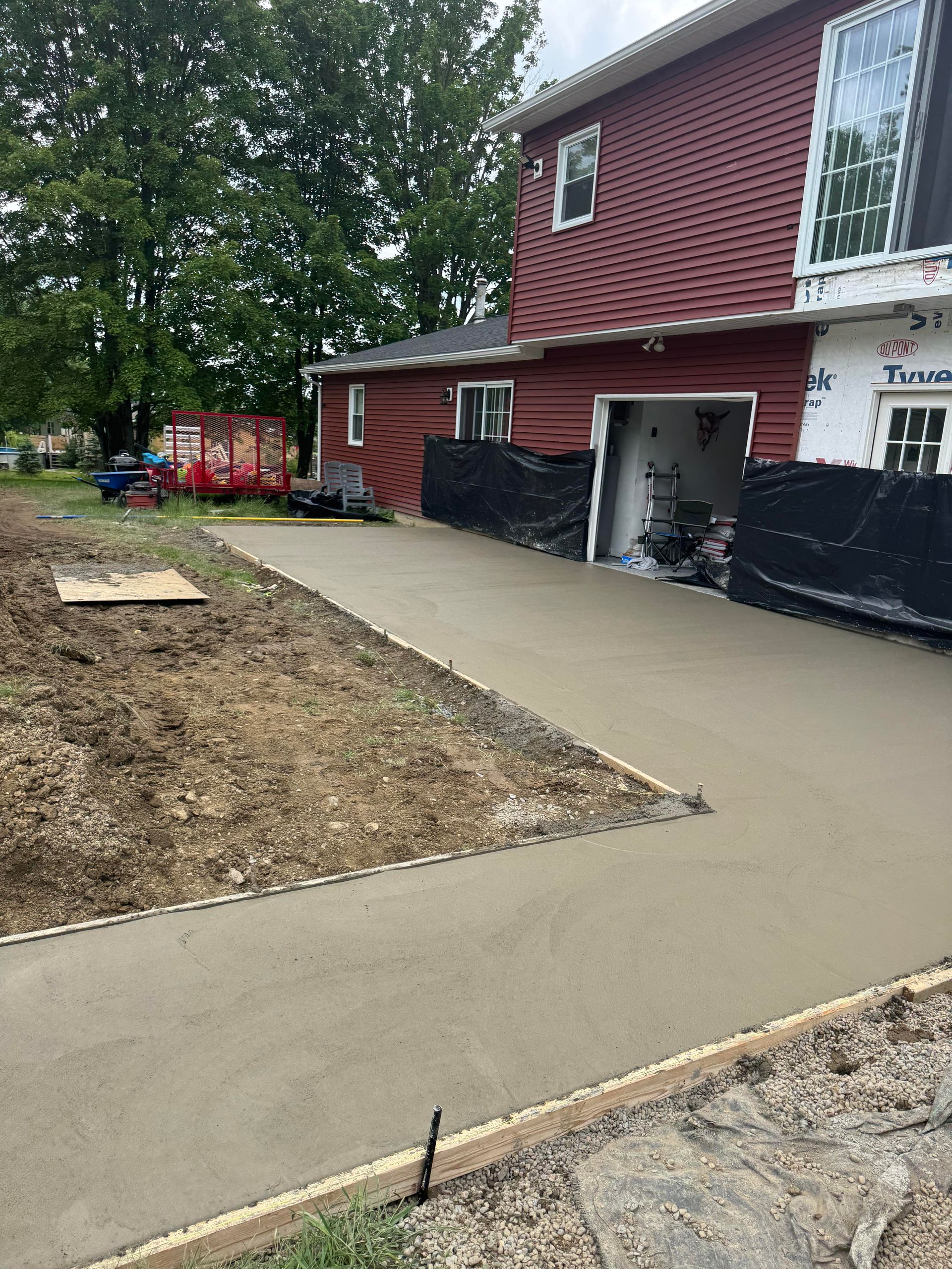 Newly poured concrete driveway with a red house and garage in the background.