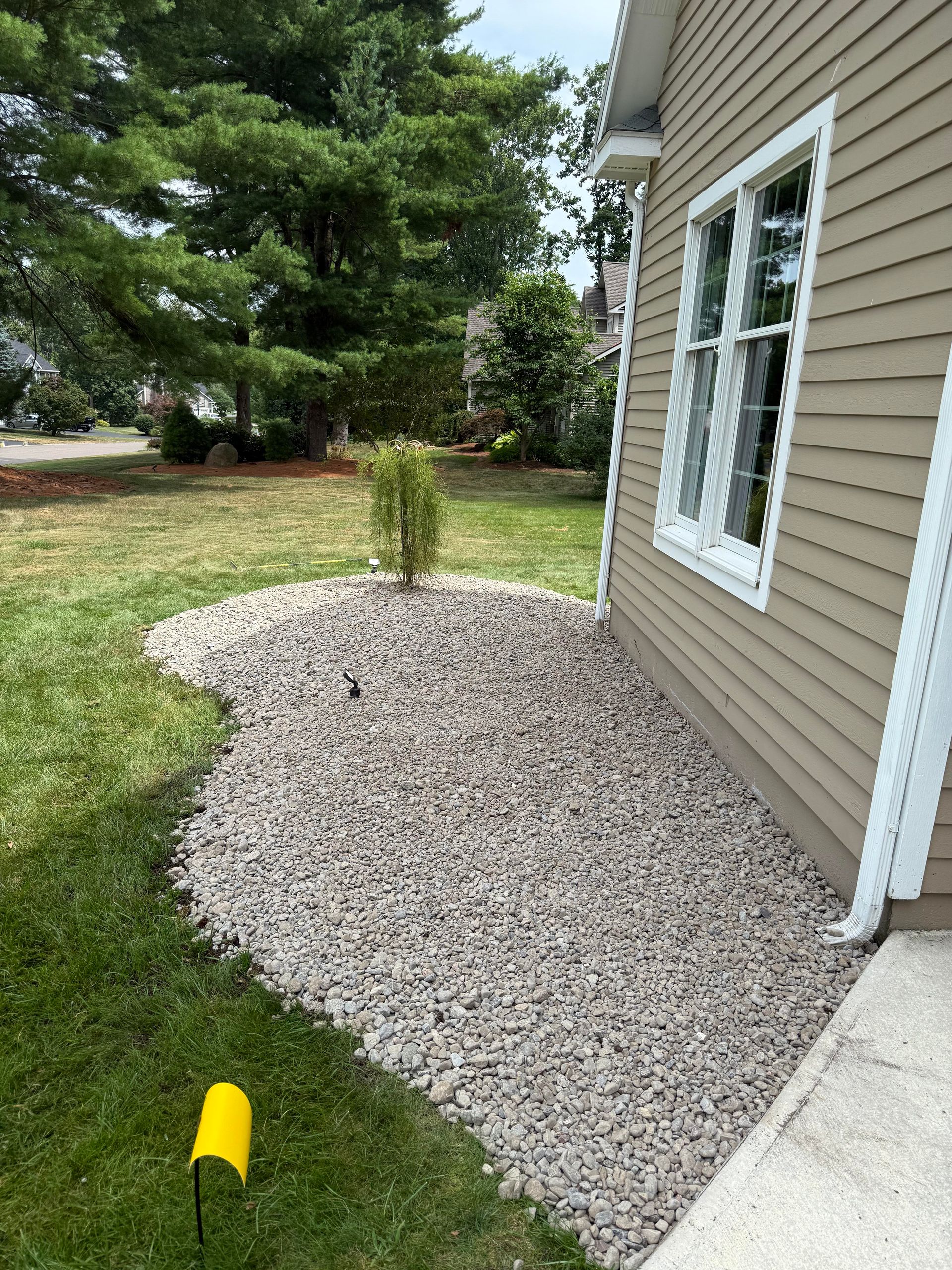 A house exterior with gravel landscaping and a small bush. Green grass is on the left.