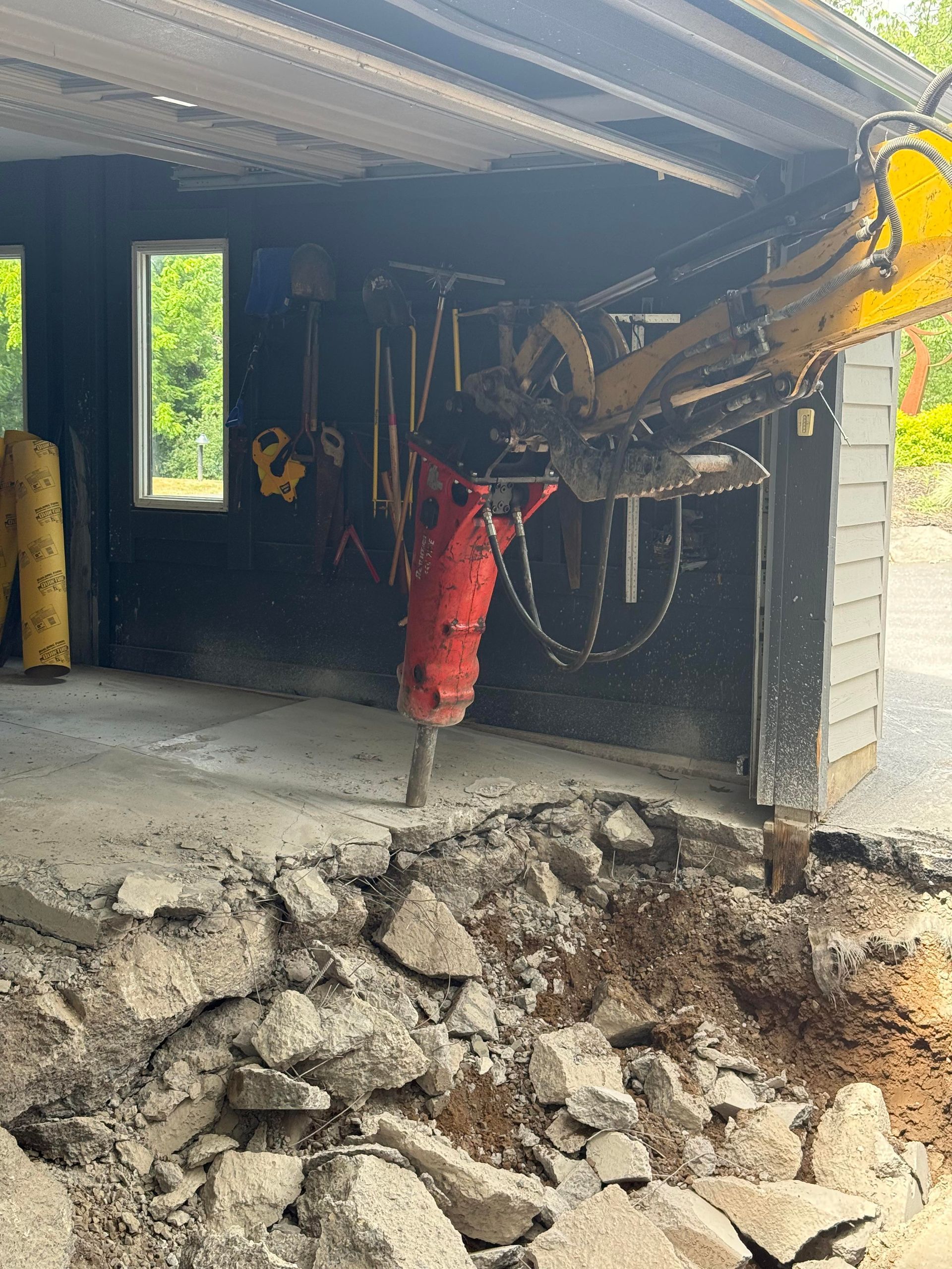 A hydraulic hammer attached to a yellow excavator demolishes concrete near a building.