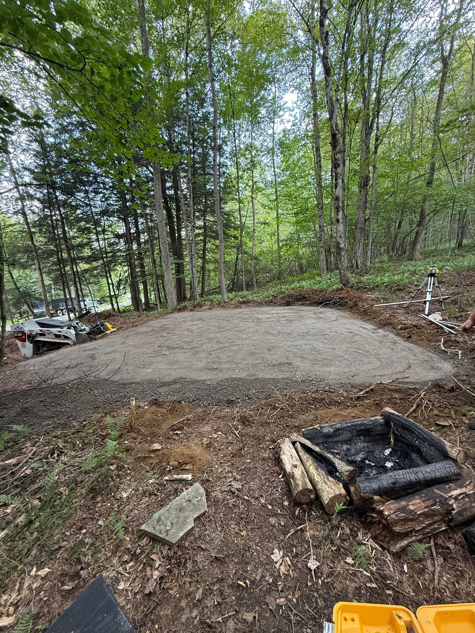 A leveled gravel area in a wooded area, with fire pit in foreground.