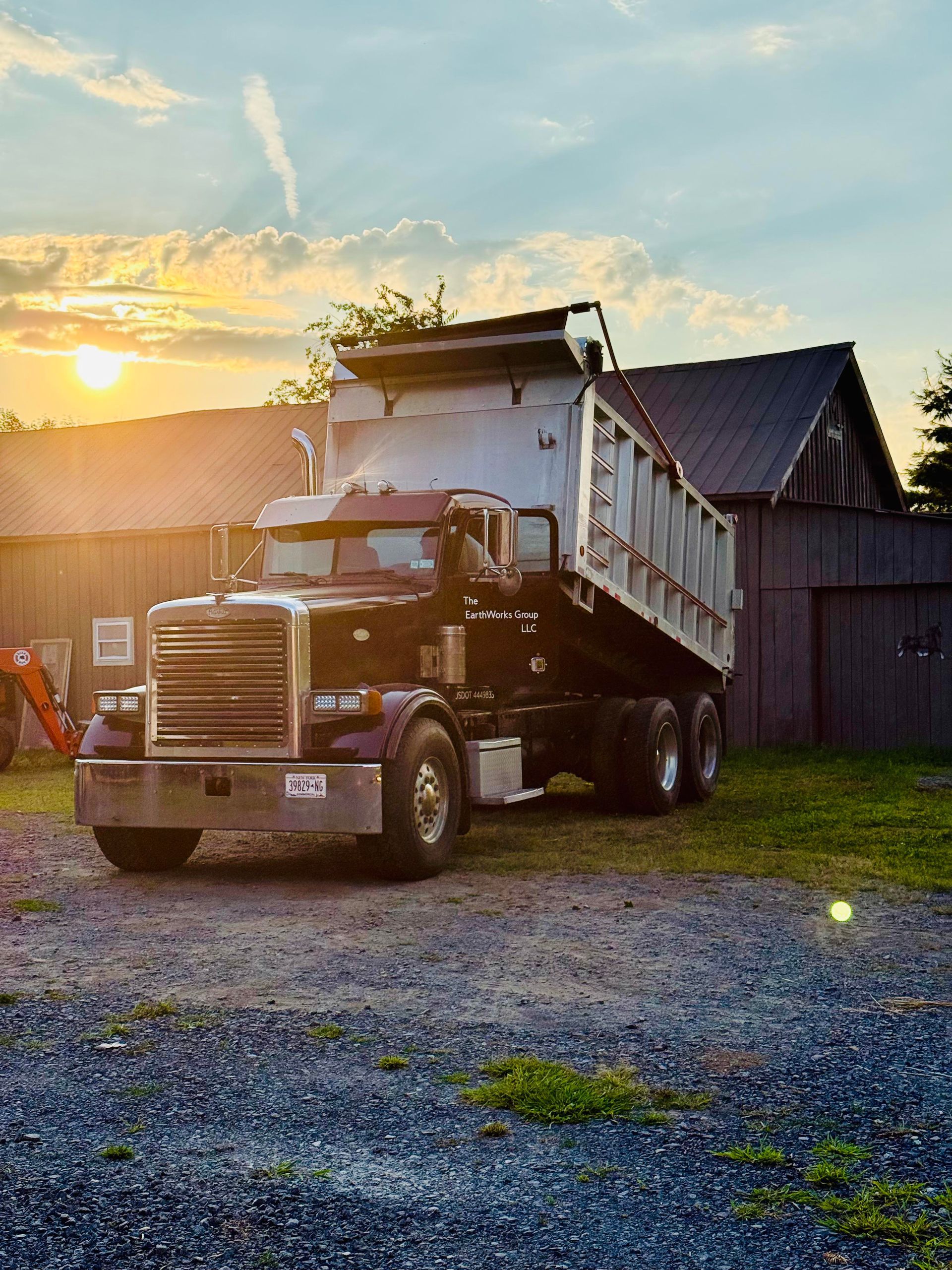 Black dump truck with raised bed against a sunset and wooden barn.