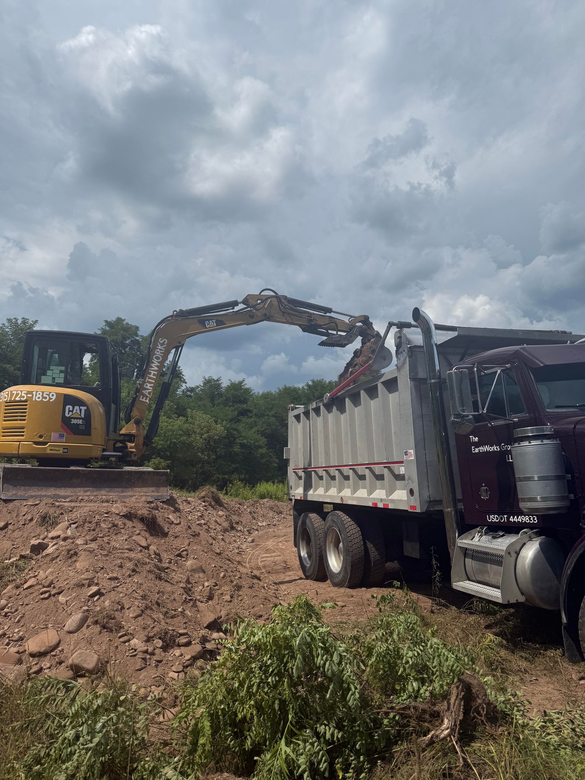 Excavator loading a dump truck with dirt on a construction site under a cloudy sky.