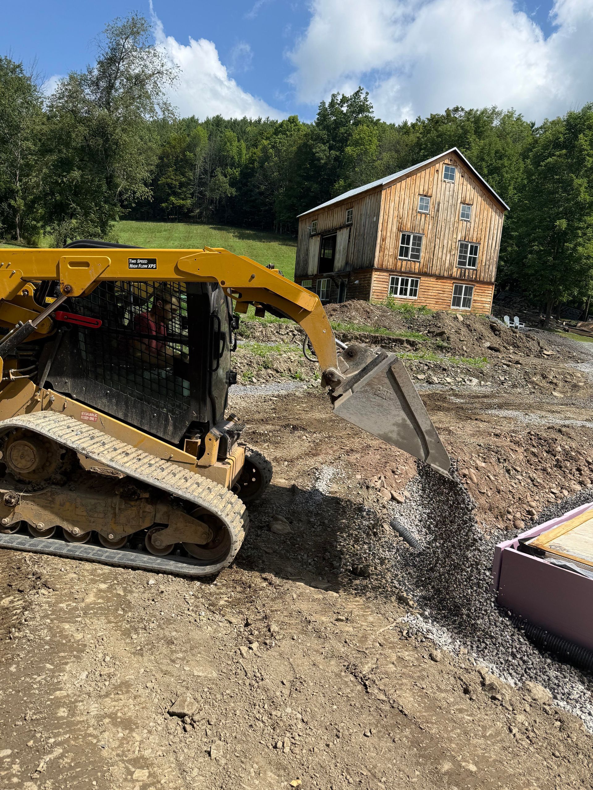 Yellow bulldozer leveling ground near a wooden building under a sunny sky.