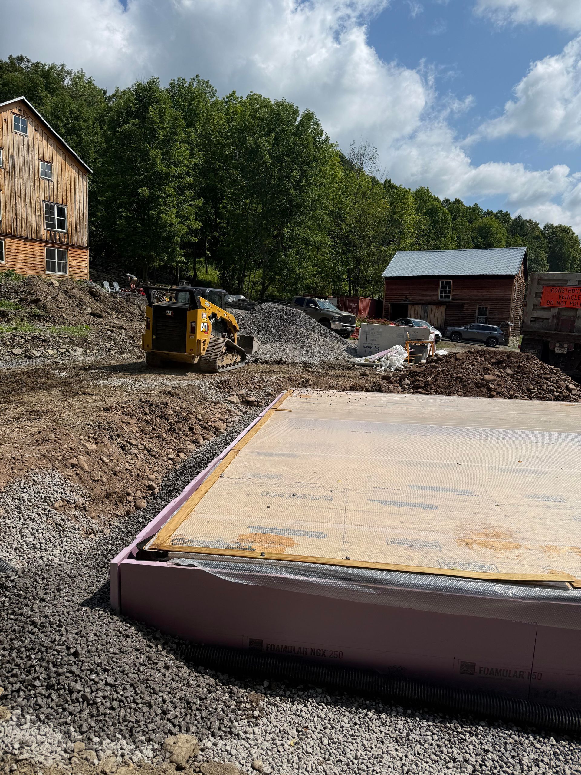 Construction site with a new foundation, a small tractor, and an old barn.