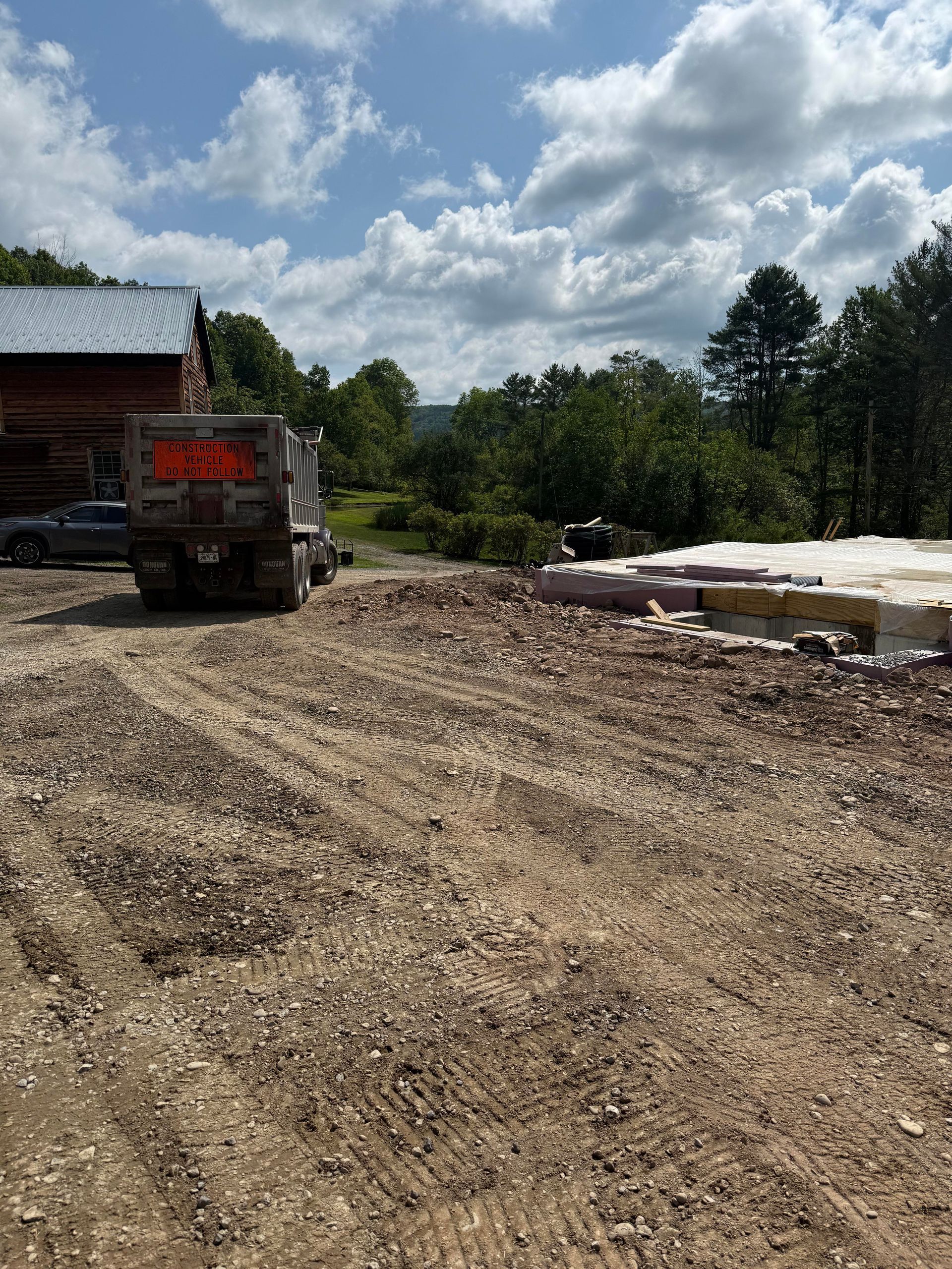 Truck parked on gravel lot near a building. Construction materials and trees are also visible.