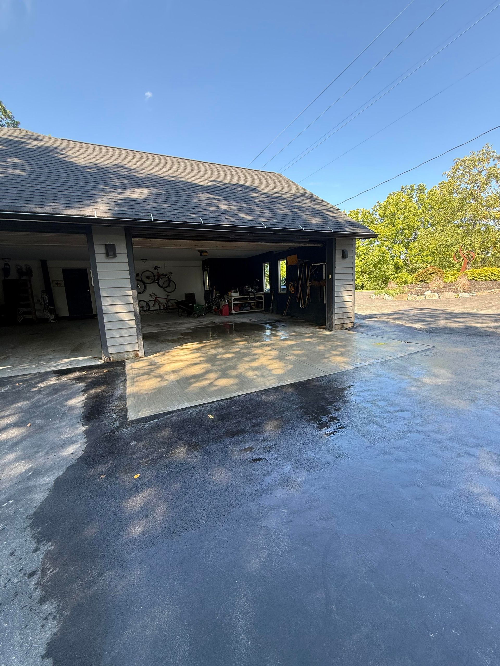 Garage with open door, dark roof, asphalt driveway, clear sky.