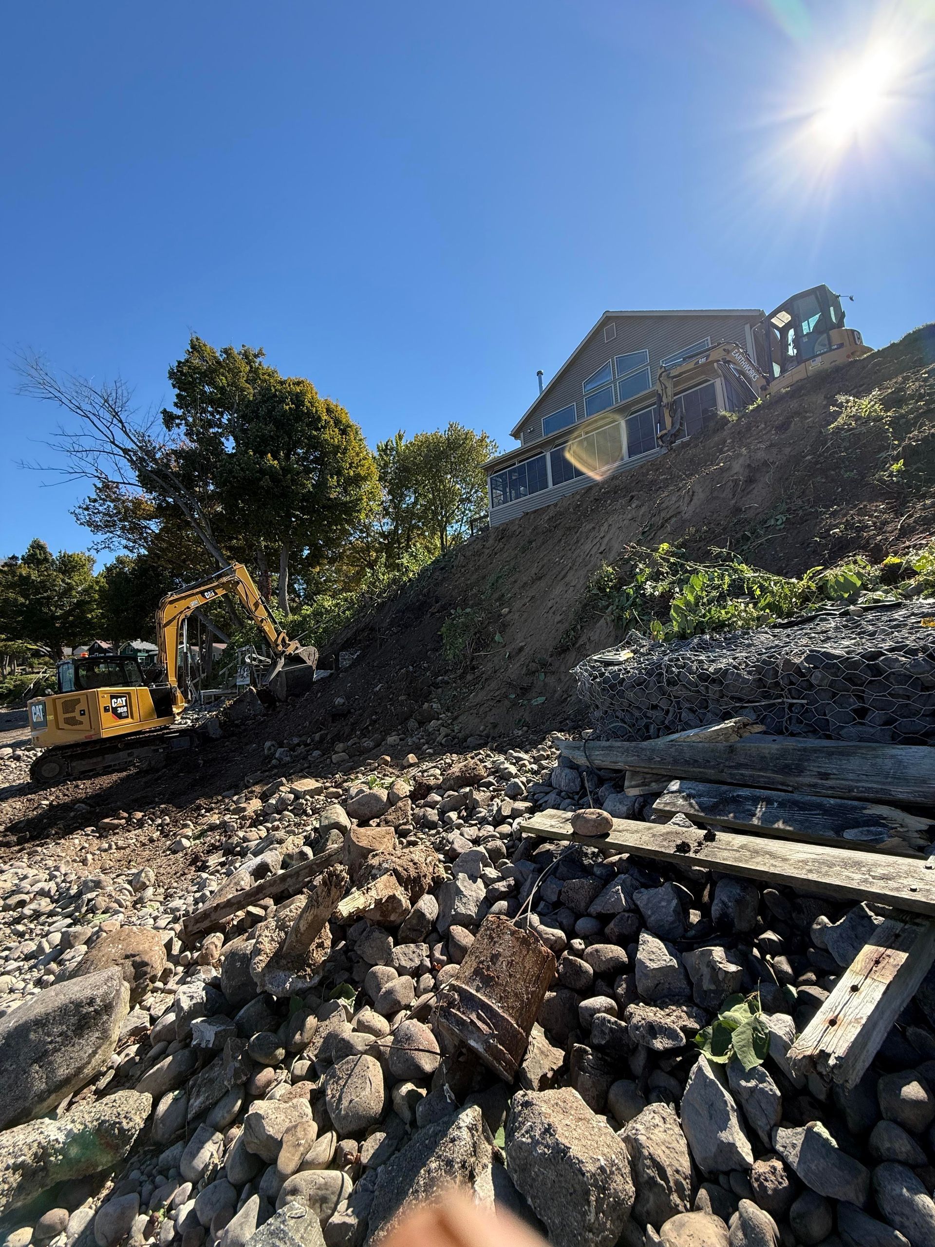 Construction site with excavators moving earth near a building under a sunny sky.