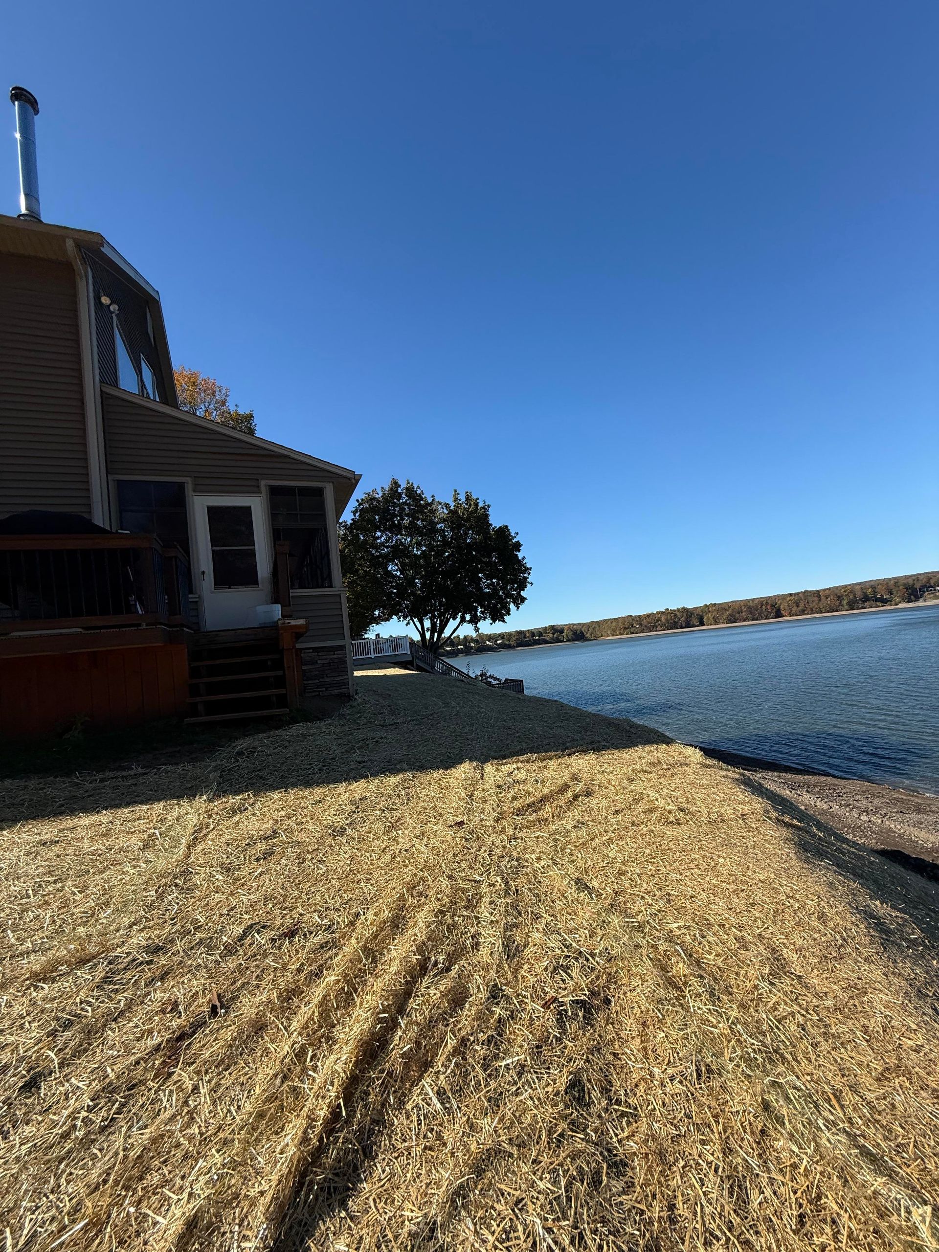 House by a lake with wood chip ground cover. Blue sky.