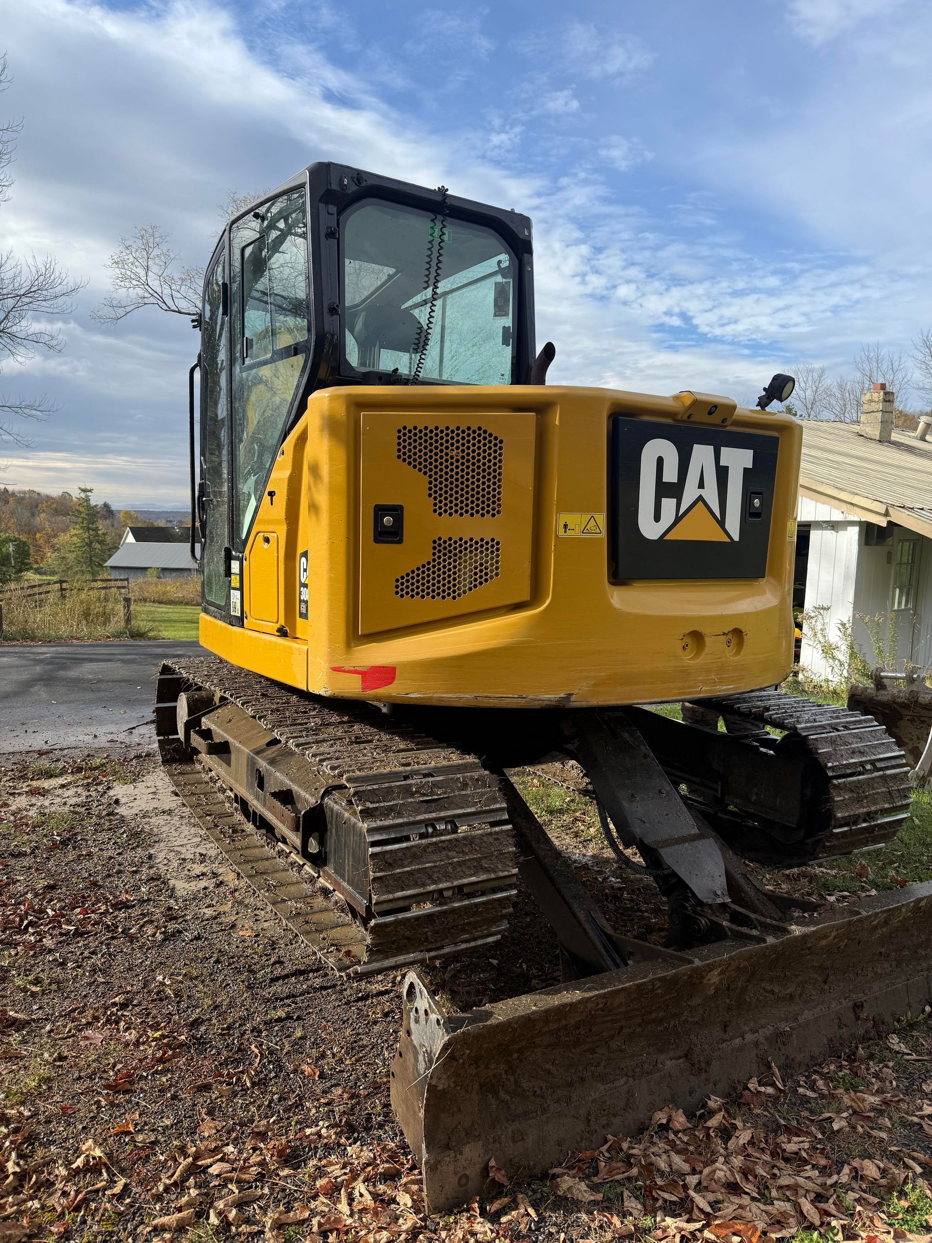 Yellow Caterpillar mini excavator on a gravel surface with a cloudy sky backdrop.