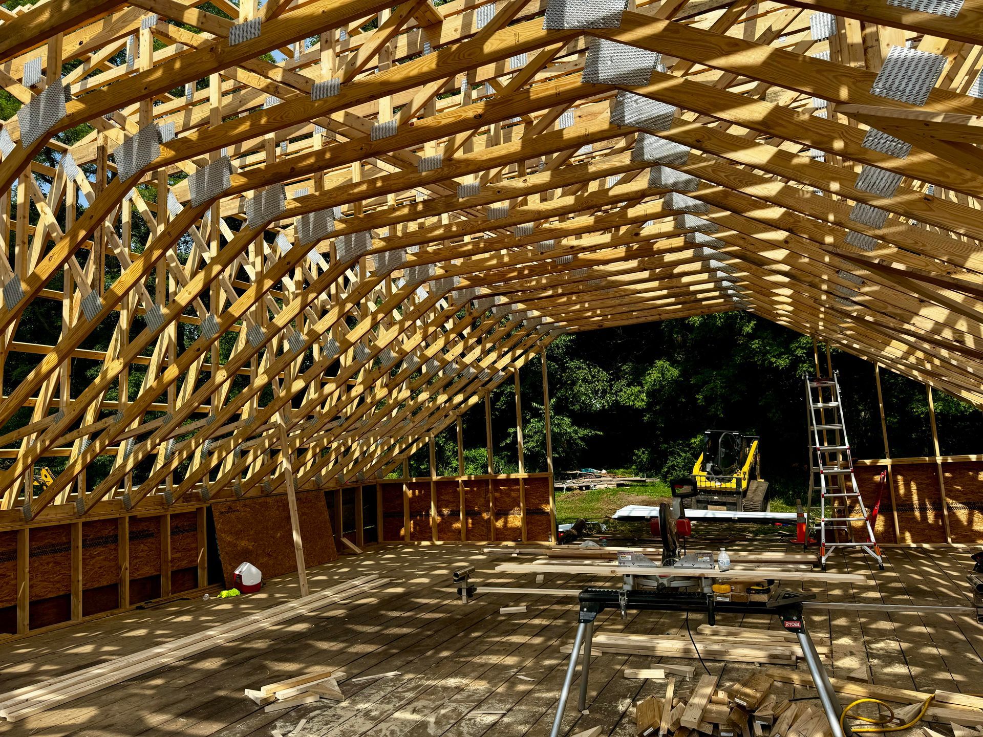 Interior view of a wooden building under construction, with visible rafters, trusses, and partial walls.
