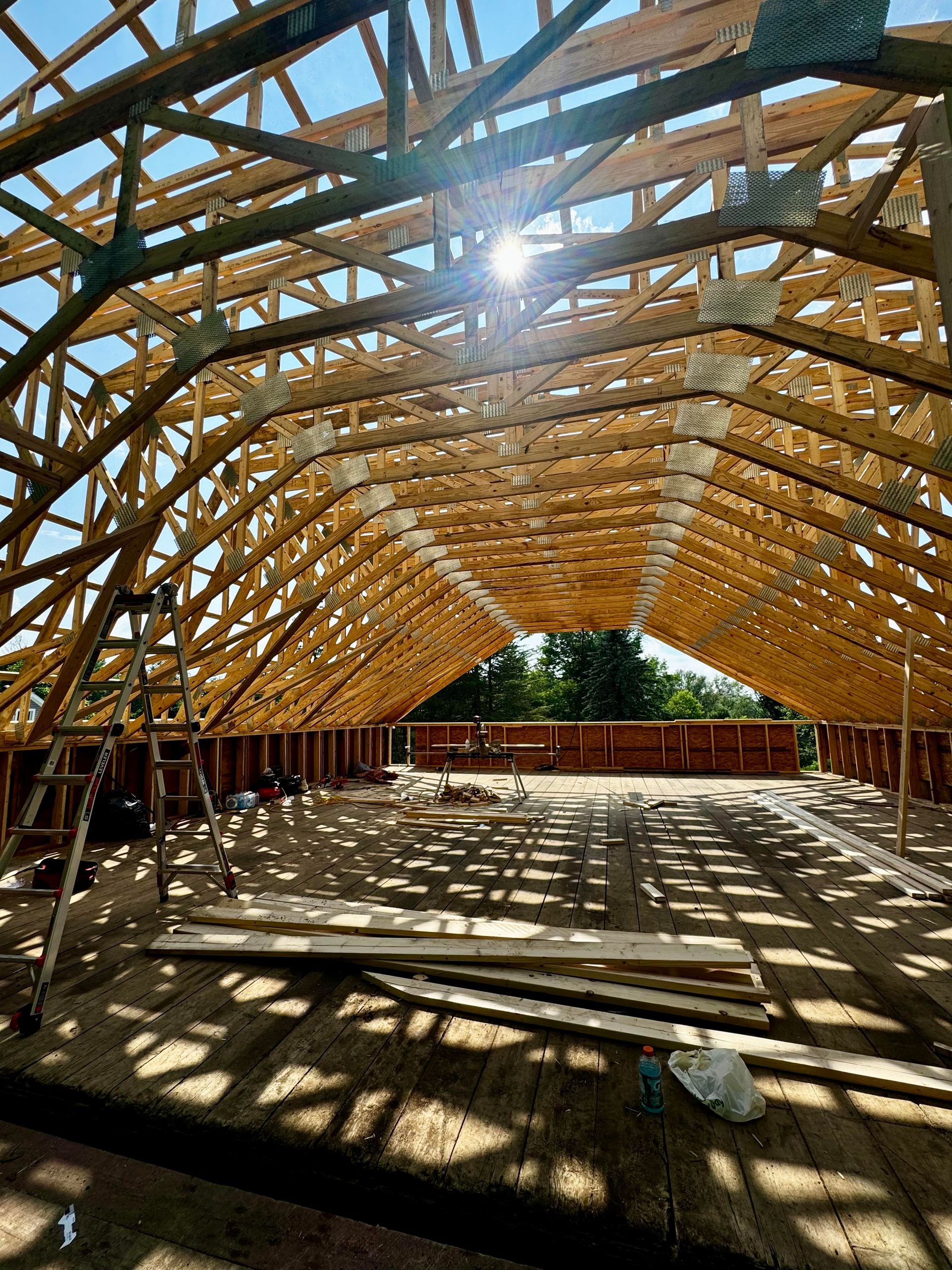 Wooden framework of a building under construction, arched roof, sunlight streaming through.
