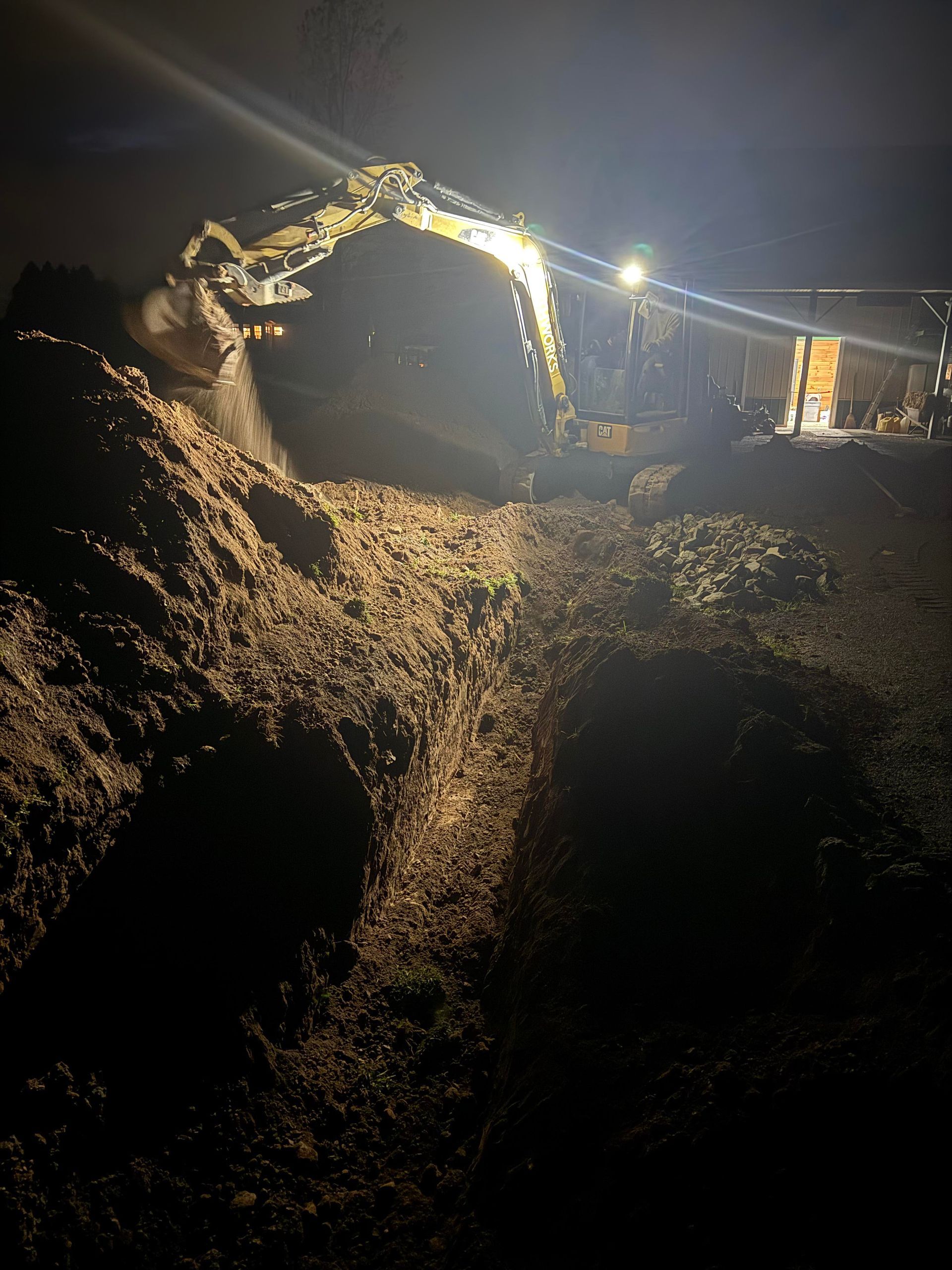 Excavator digging at night, illuminated by bright lights, moving earth.