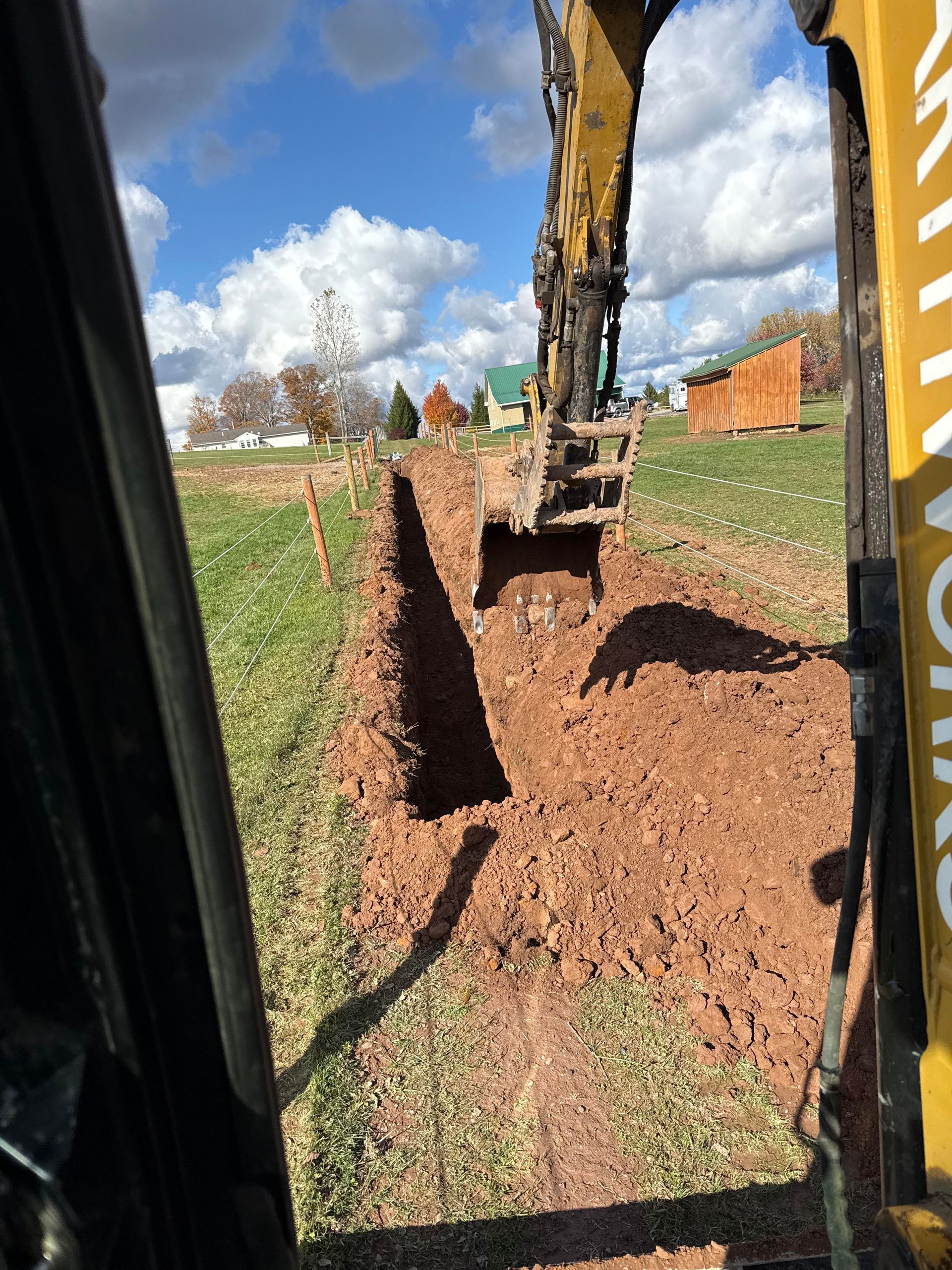 Excavator digging a trench in a grassy field on a sunny day.