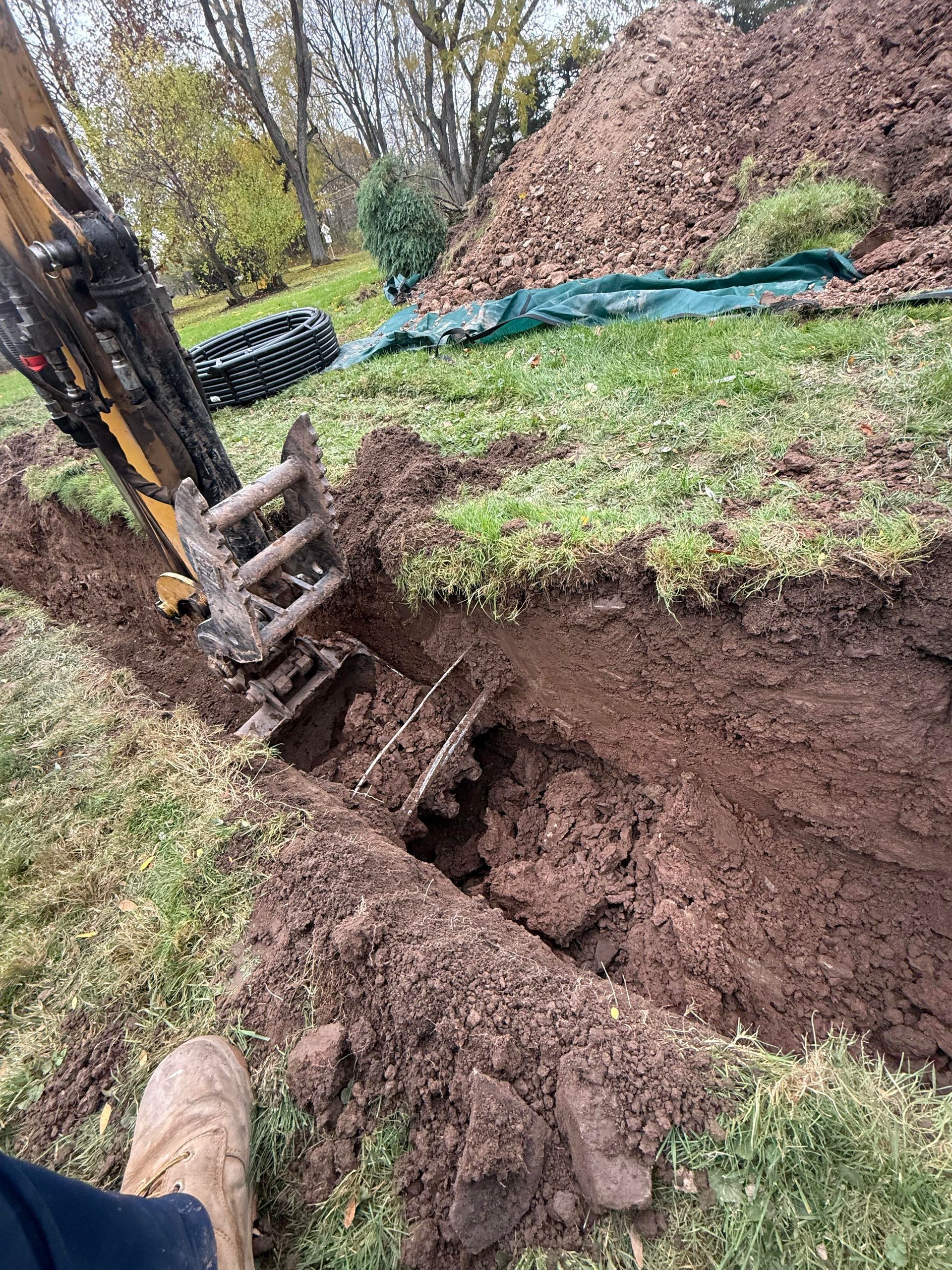An excavator digging a trench in a grassy yard, brown soil, with a pile of dirt in the background.