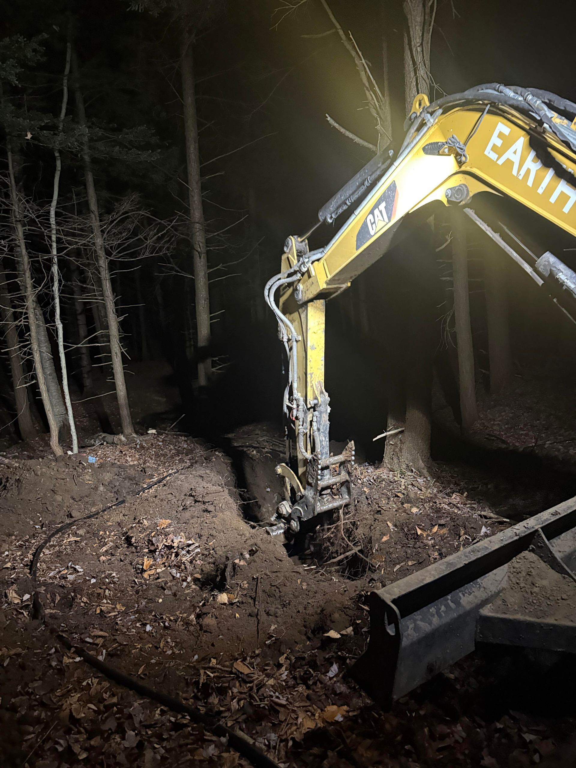 Yellow excavator digging a trench in a dark forest at night.
