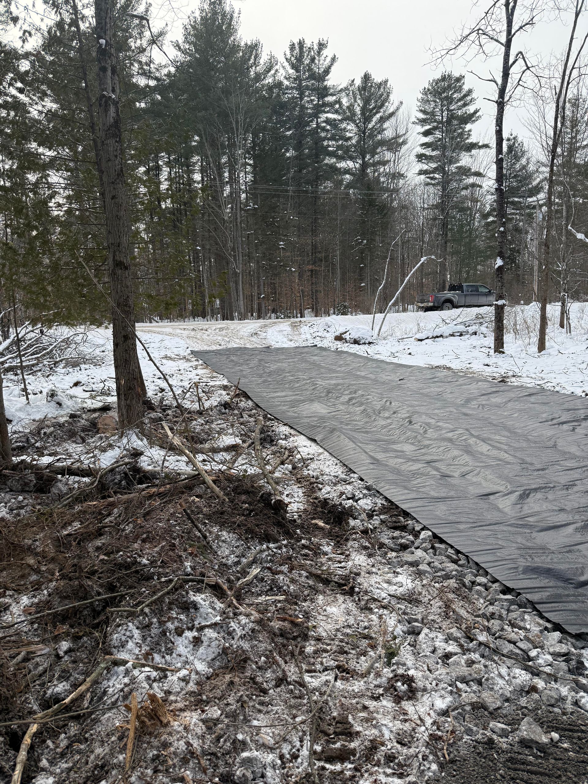 A snowy landscape with a black tarp covering a path. A truck is parked in the distance.