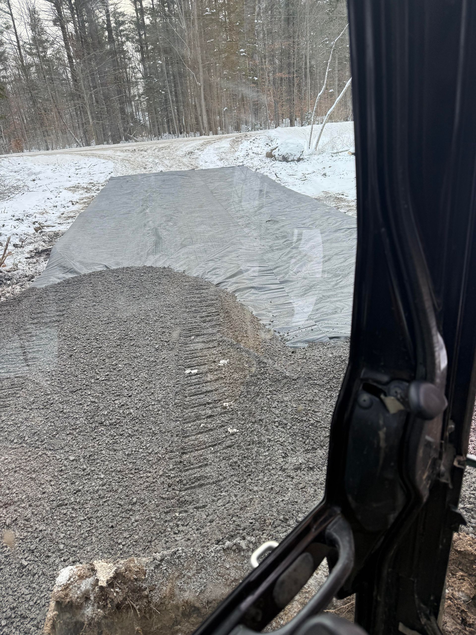 Gravel pile in front of a snow-covered field, viewed from inside a vehicle.