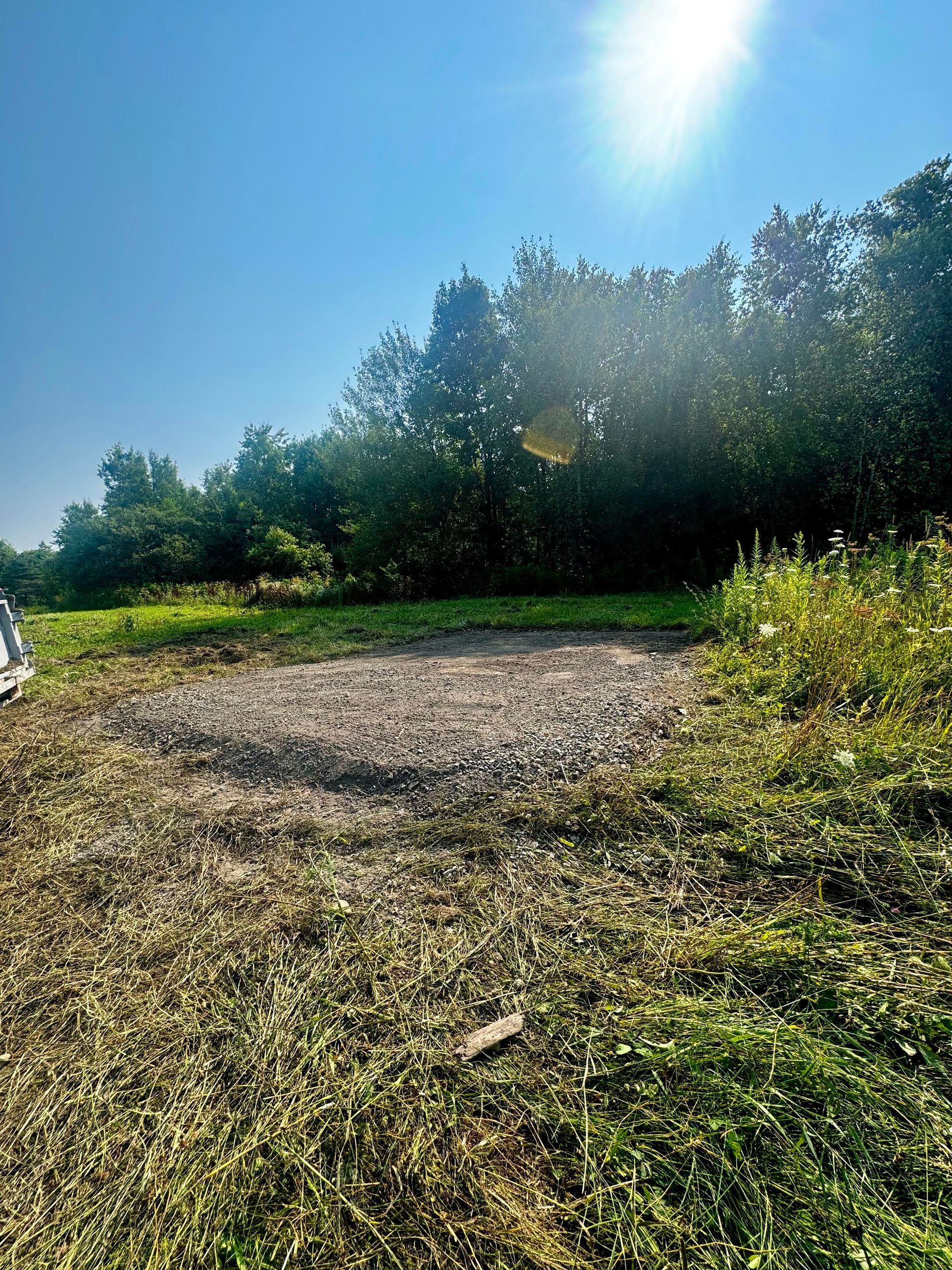 Gravel patch in a grassy area with trees and bright sun.