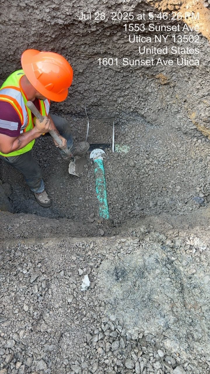 Construction worker in orange hard hat works on green pipe in a trench.