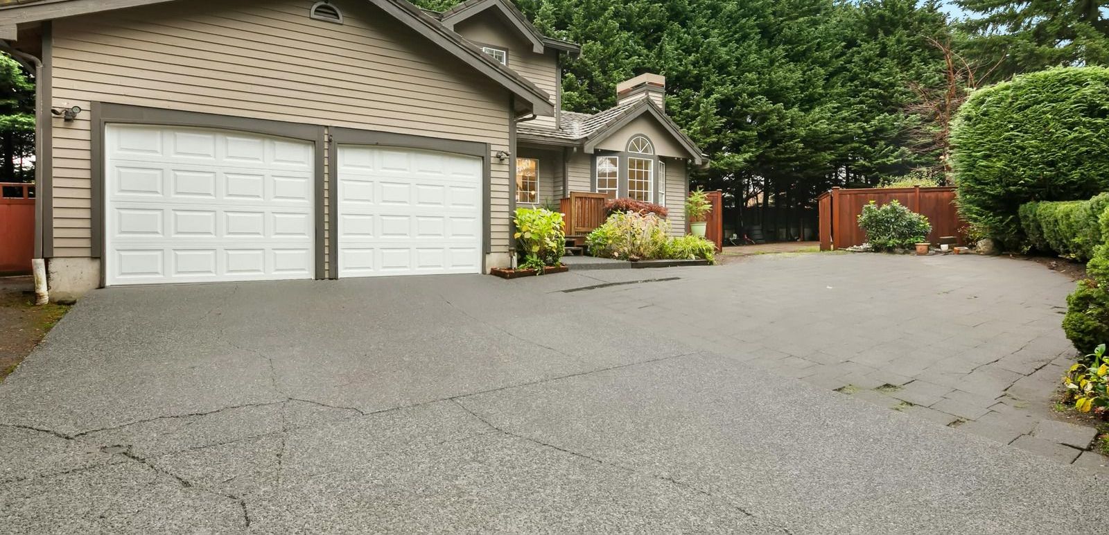House with a two-car garage and a driveway surrounded by trees.