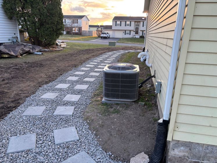 An air conditioner is sitting on the side of a house next to a walkway.