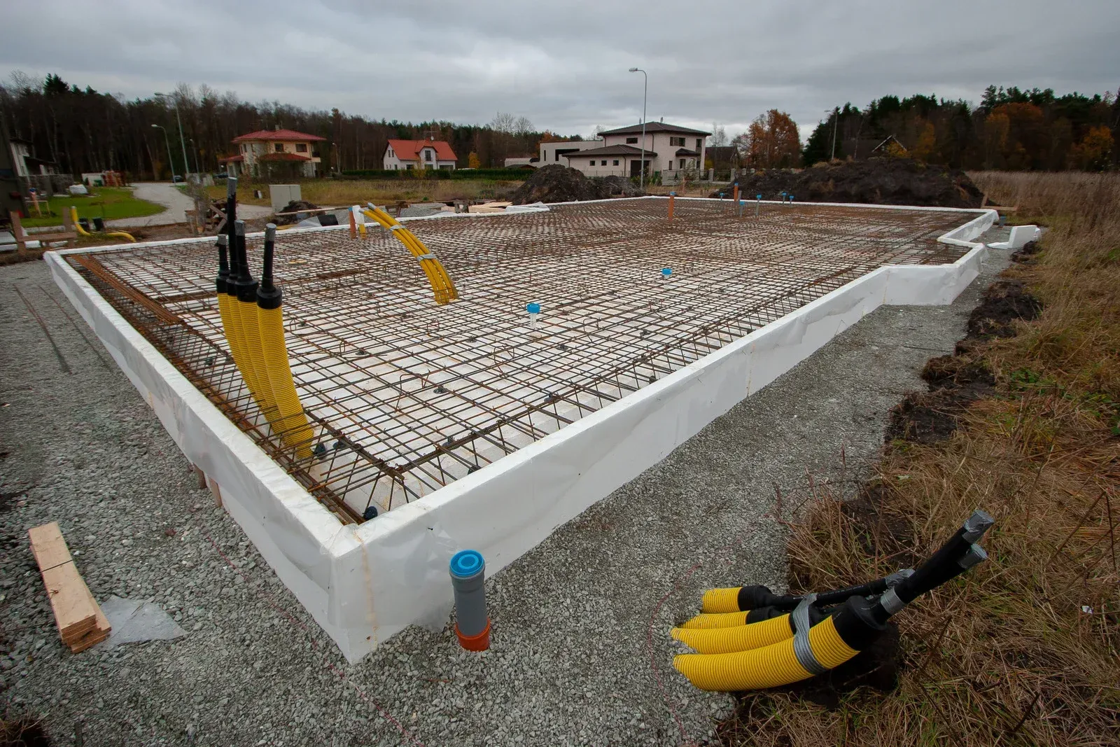 Foundation of a house under construction, showing rebar grid, yellow conduits, and white insulation.