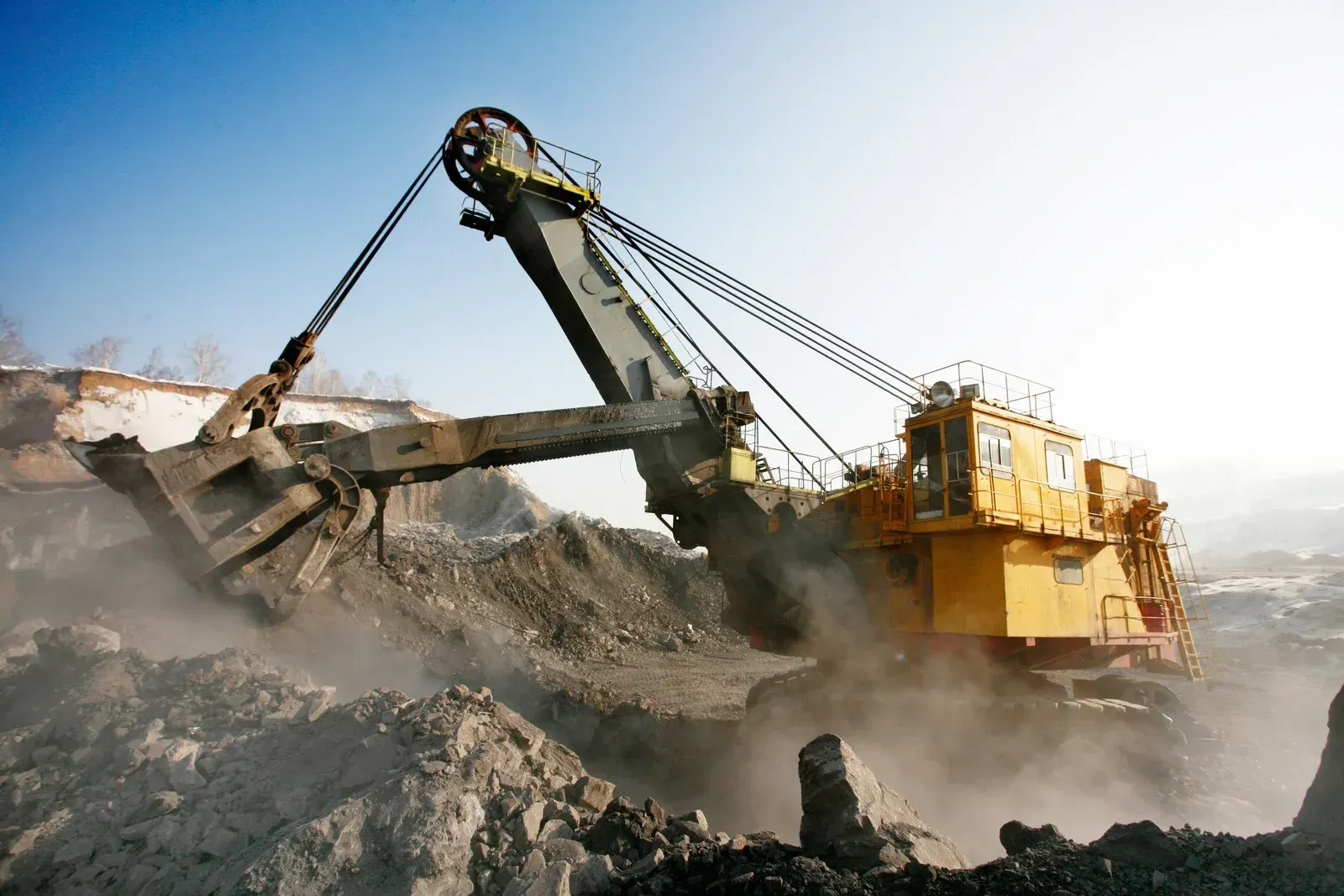 Yellow mining excavator scoops dirt in an outdoor setting, against a blue sky.