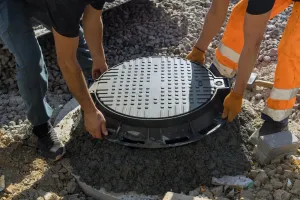 Two men are working on a manhole cover on the ground.