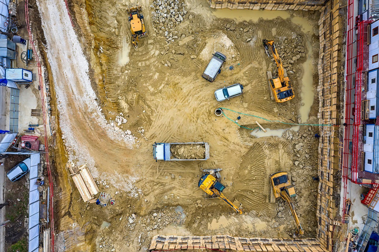 Aerial view of a construction site: Excavated earth with trucks, excavators, and building materials.