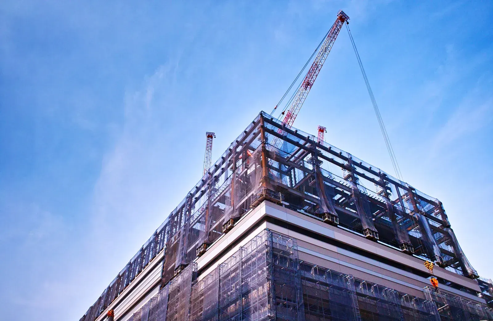 Building under construction, crane overhead, against a blue sky.