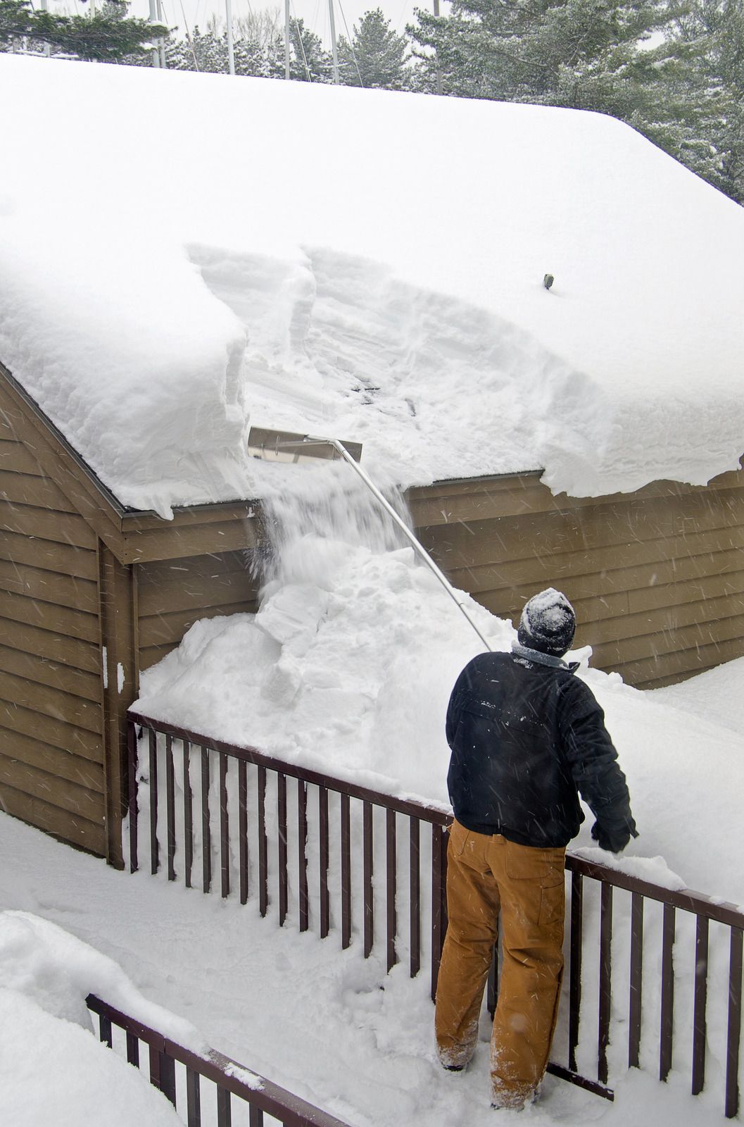A man is clearing snow from the roof of a building