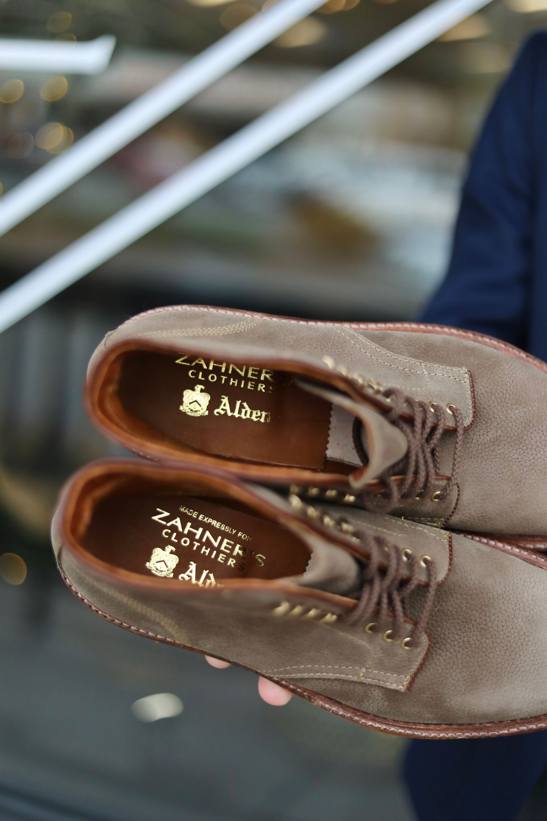 A person is holding a pair of brown shoes that say alden