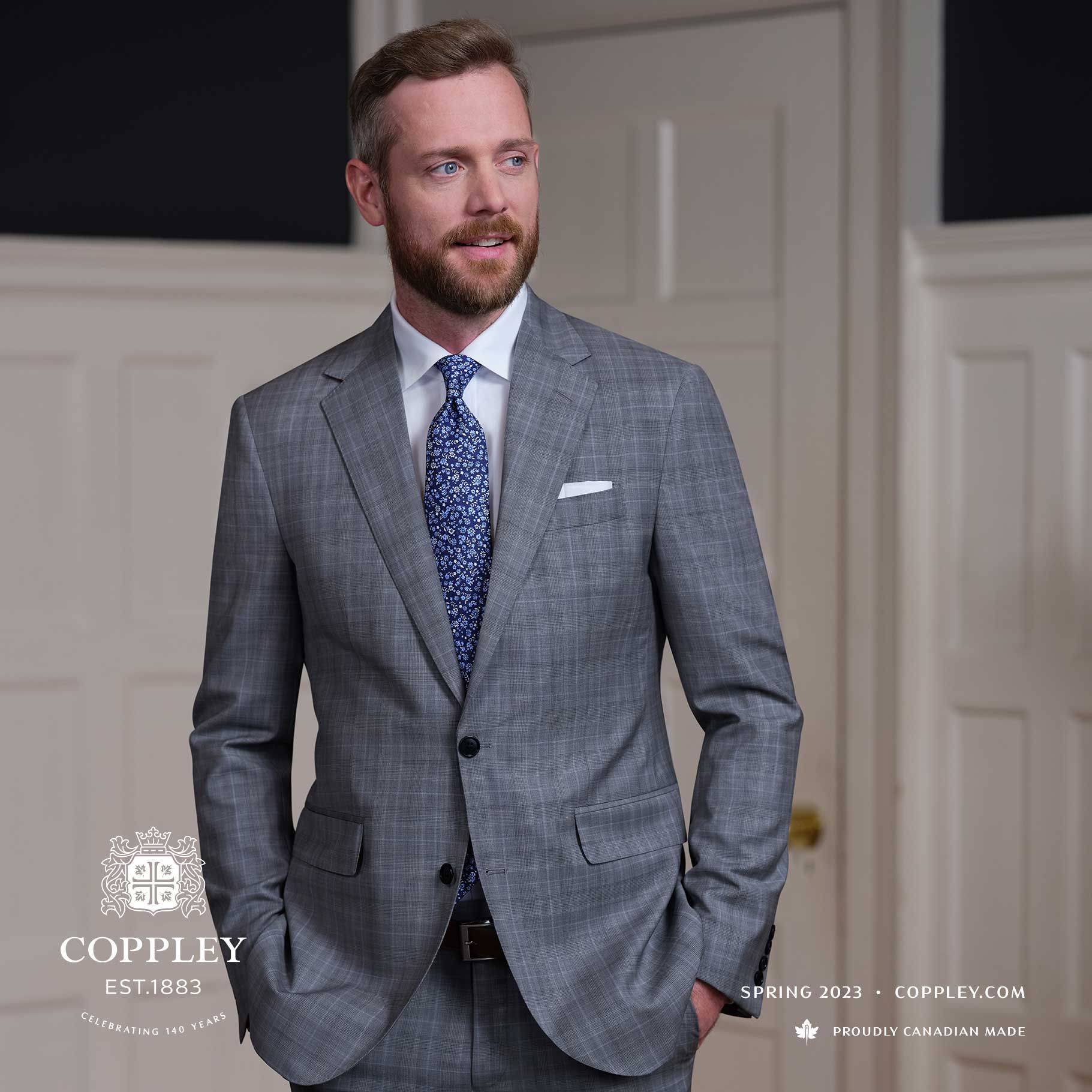 A man in a grey suit and tie is standing with his hands in his pockets