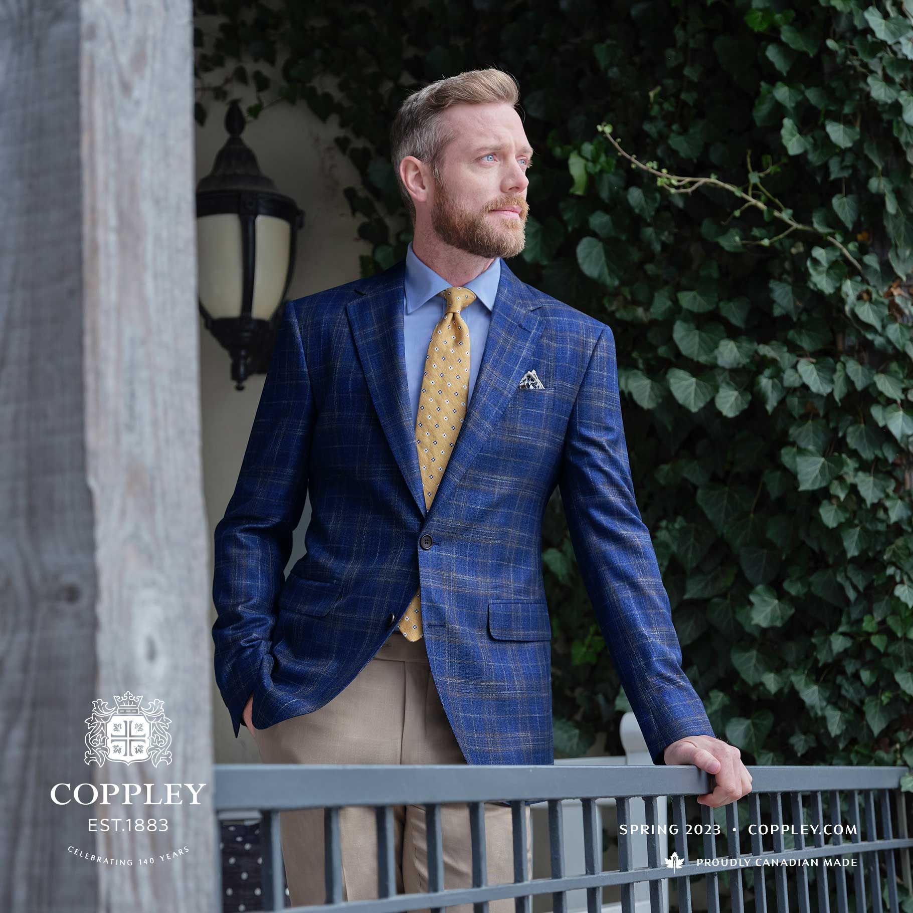 A man in a blue suit and yellow tie is leaning on a railing