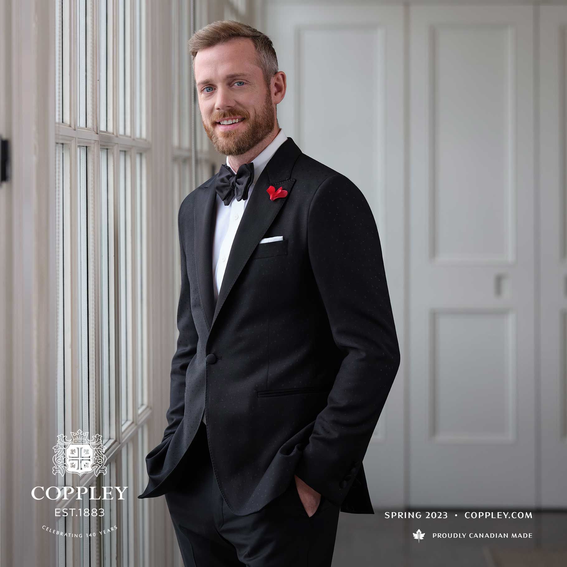 A man in a tuxedo and bow tie is standing in front of a window.