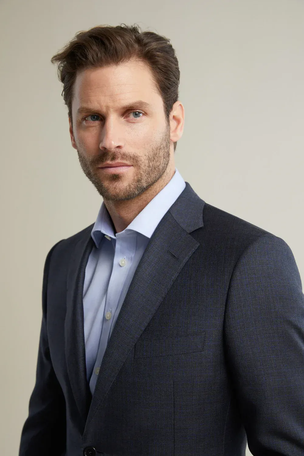 A man with a beard is wearing a suit and a blue shirt.