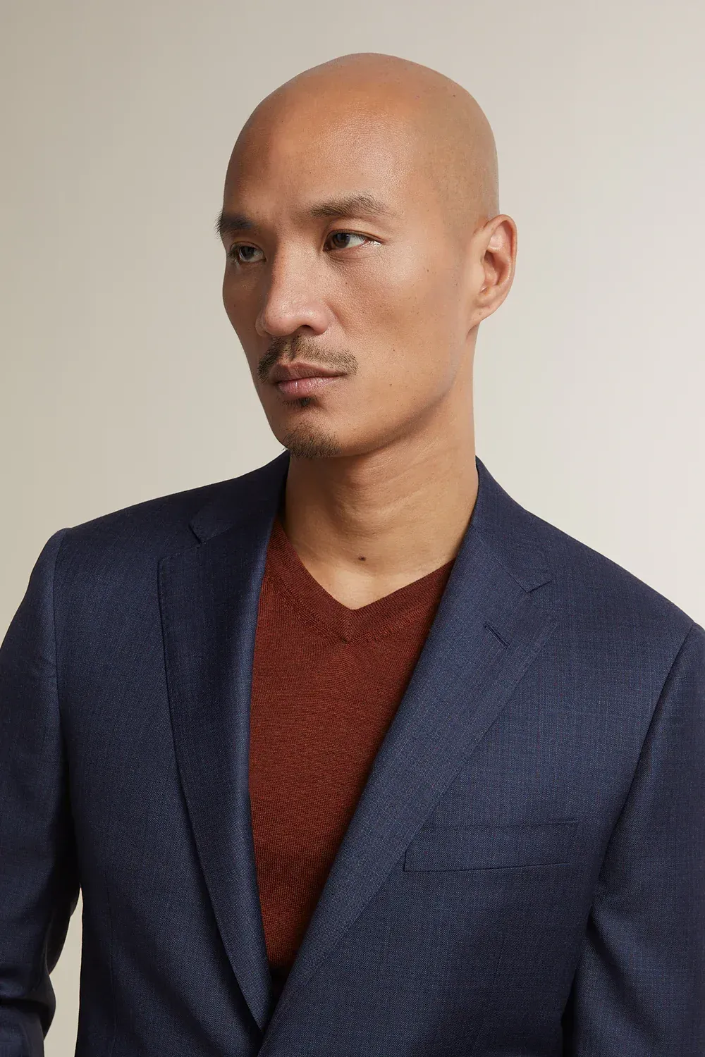 A bald man is wearing a blue suit jacket and a red sweater.