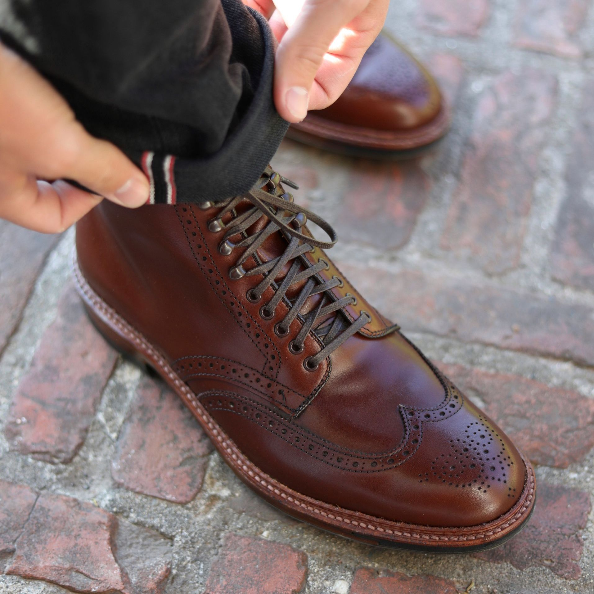 A person is tying a pair of brown brogue boots