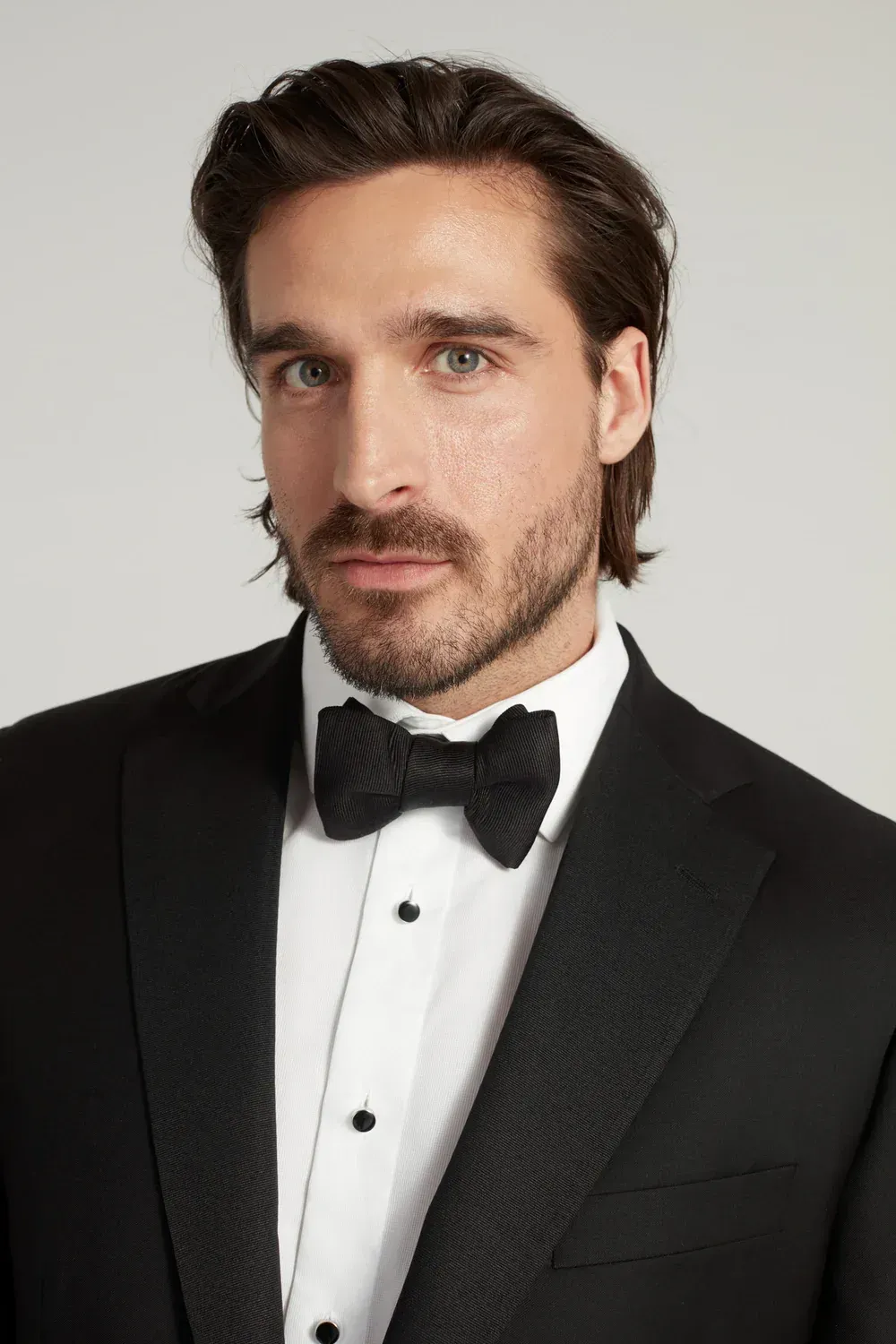 A man in a tuxedo and bow tie is looking at the camera.
