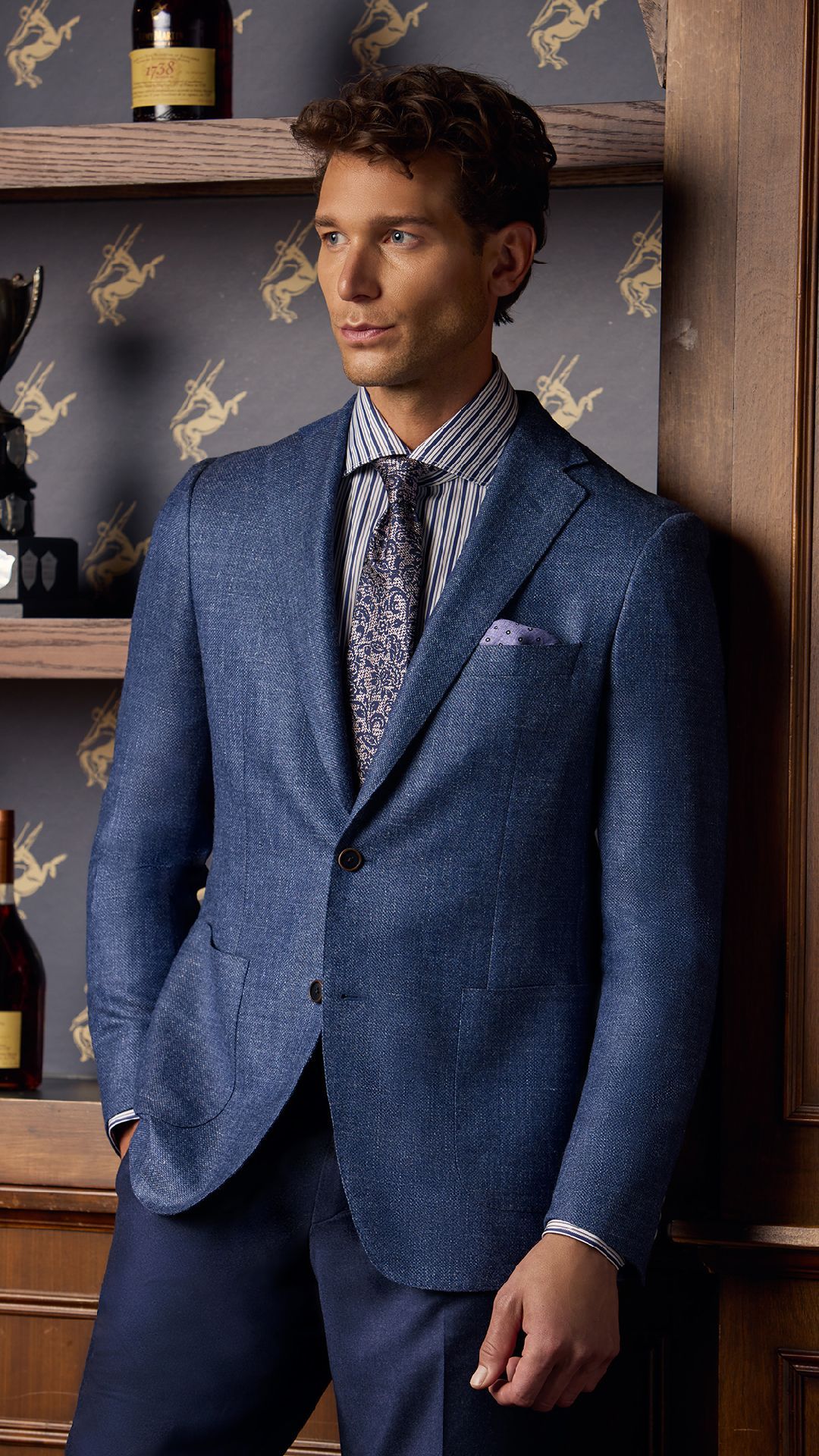 A man in a blue suit and tie is leaning against a wall.