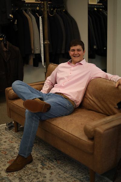 A man in a pink shirt is sitting on a brown couch.