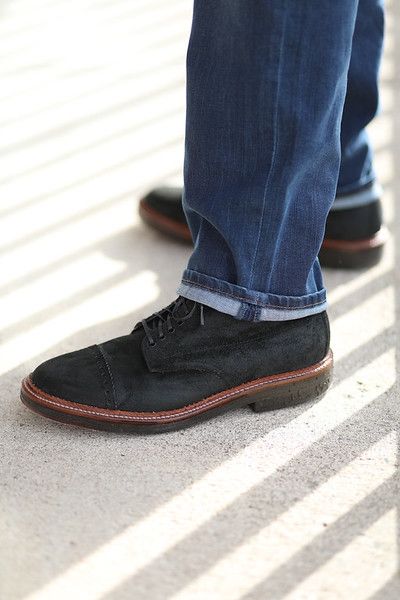 A person wearing jeans and black shoes is standing on a sidewalk.