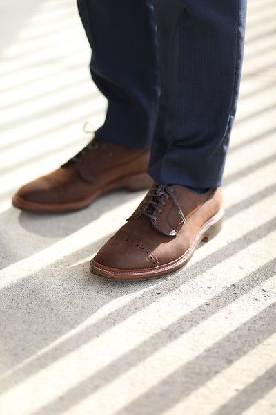 A person wearing brown shoes and blue pants is standing on a striped floor.